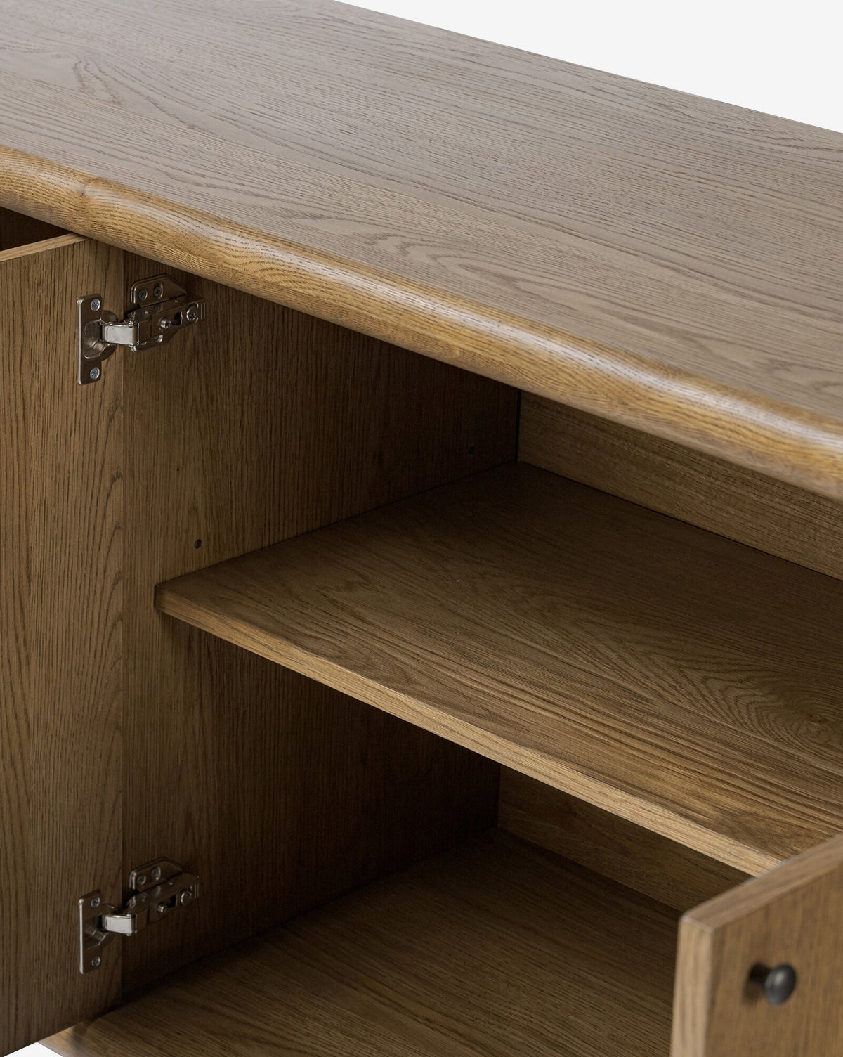 A close-up of the Rolette Sideboard reveals two interior shelves and a left-side hinged door, all made from medium-toned oak with visible grain and accented by sleek gunmetal door pulls, by McGee & Co.