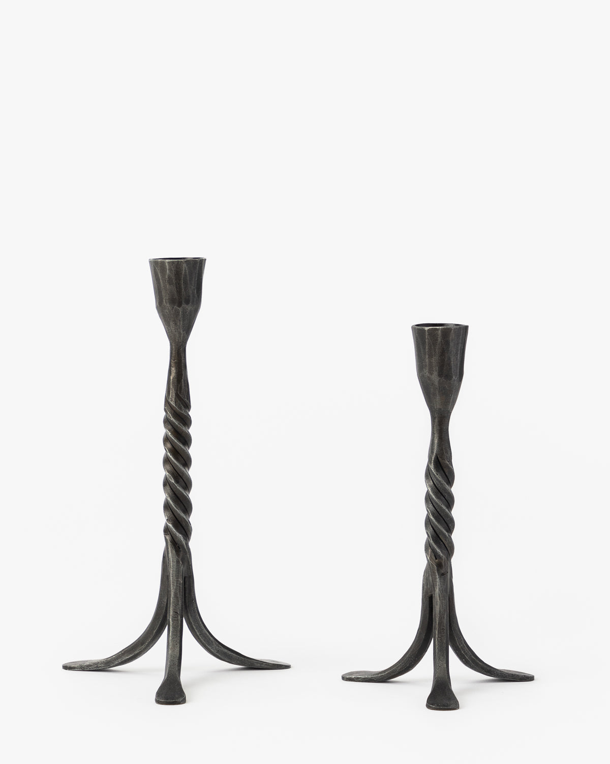 Two Rosario Taper Holders, featuring dark iron with twisted stems and sculptural tripod bases—one taller than the other—are shown on a plain white background by McGee & Co.