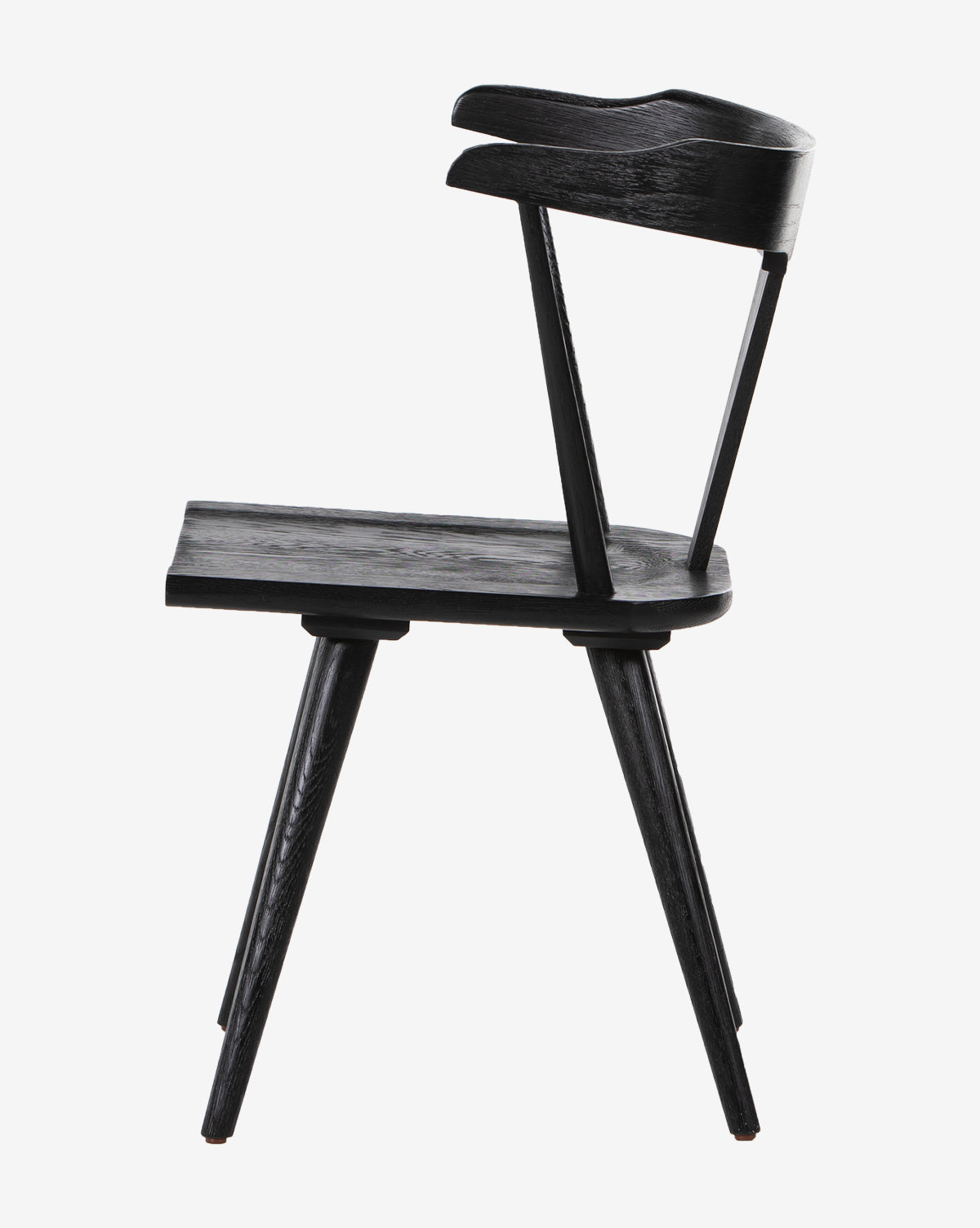 The Ruthie Dining Chair is a minimalist black solid oak chair with three legs, an angled seat, and a curved backrest, shown in profile against a white background.