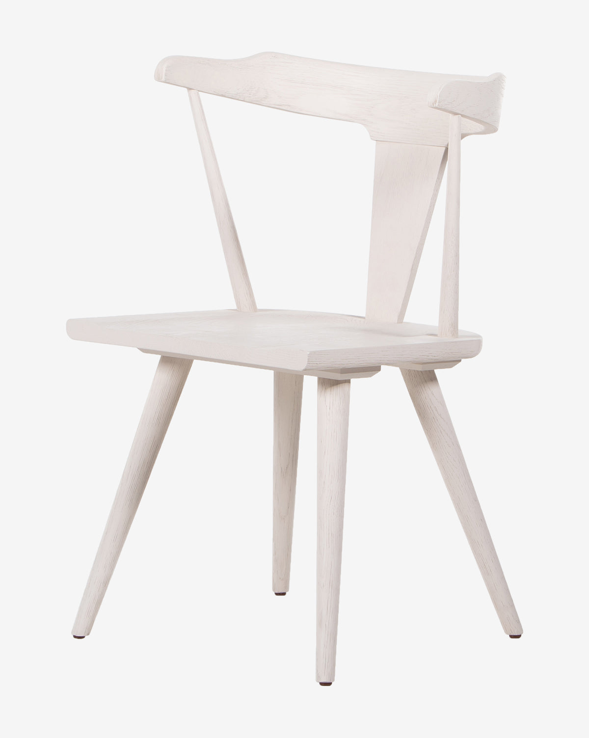 The Ruthie Dining Chair is a minimalist solid oak dining chair with a light finish, featuring a slightly curved backrest, angled back supports, and four tapered legs.