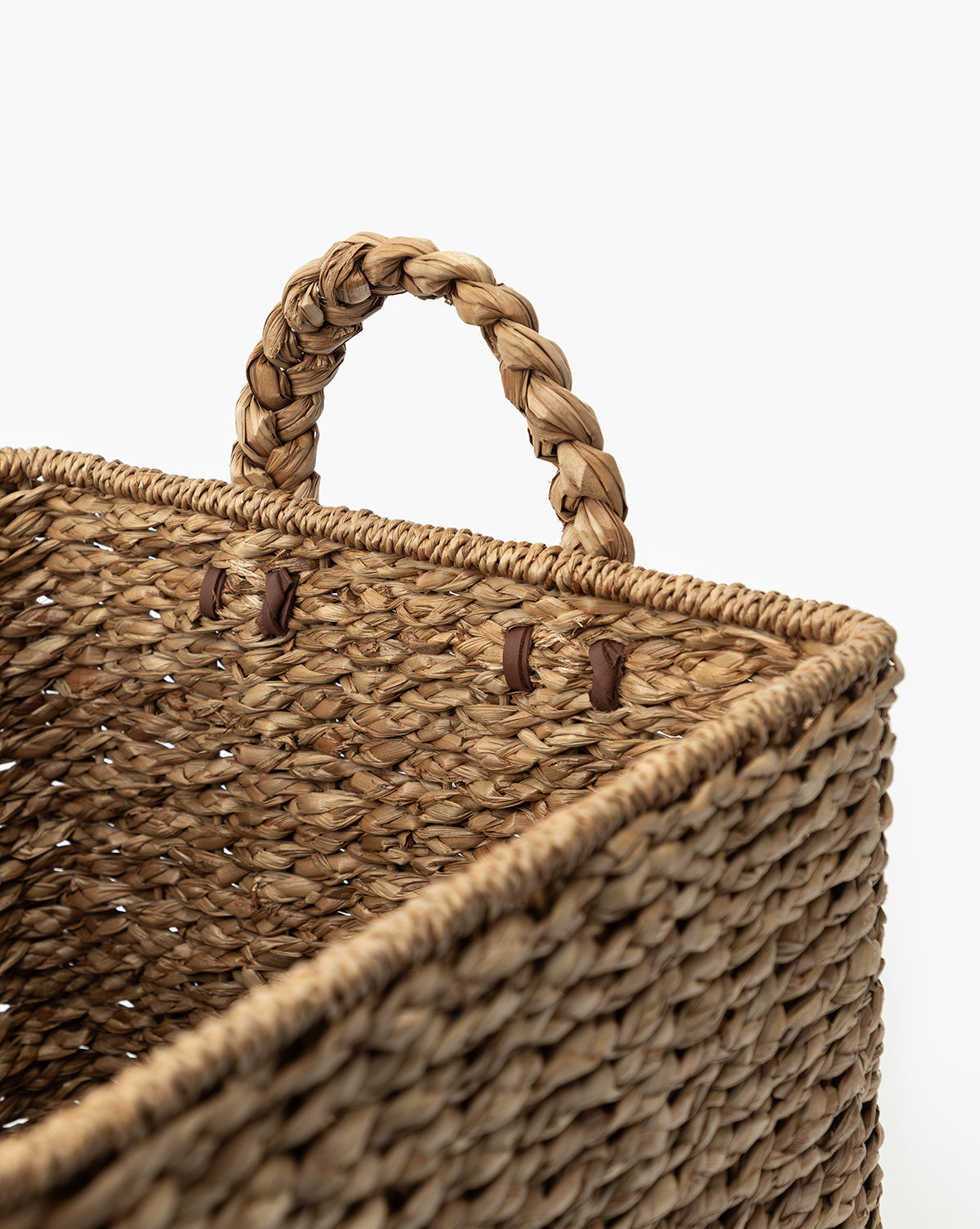 Close-up of the Salter Woven Square Basket, crafted from natural seagrass fibers with a braided handle secured by brown leather-like fasteners, shown against a plain white background, by McGee & Co.