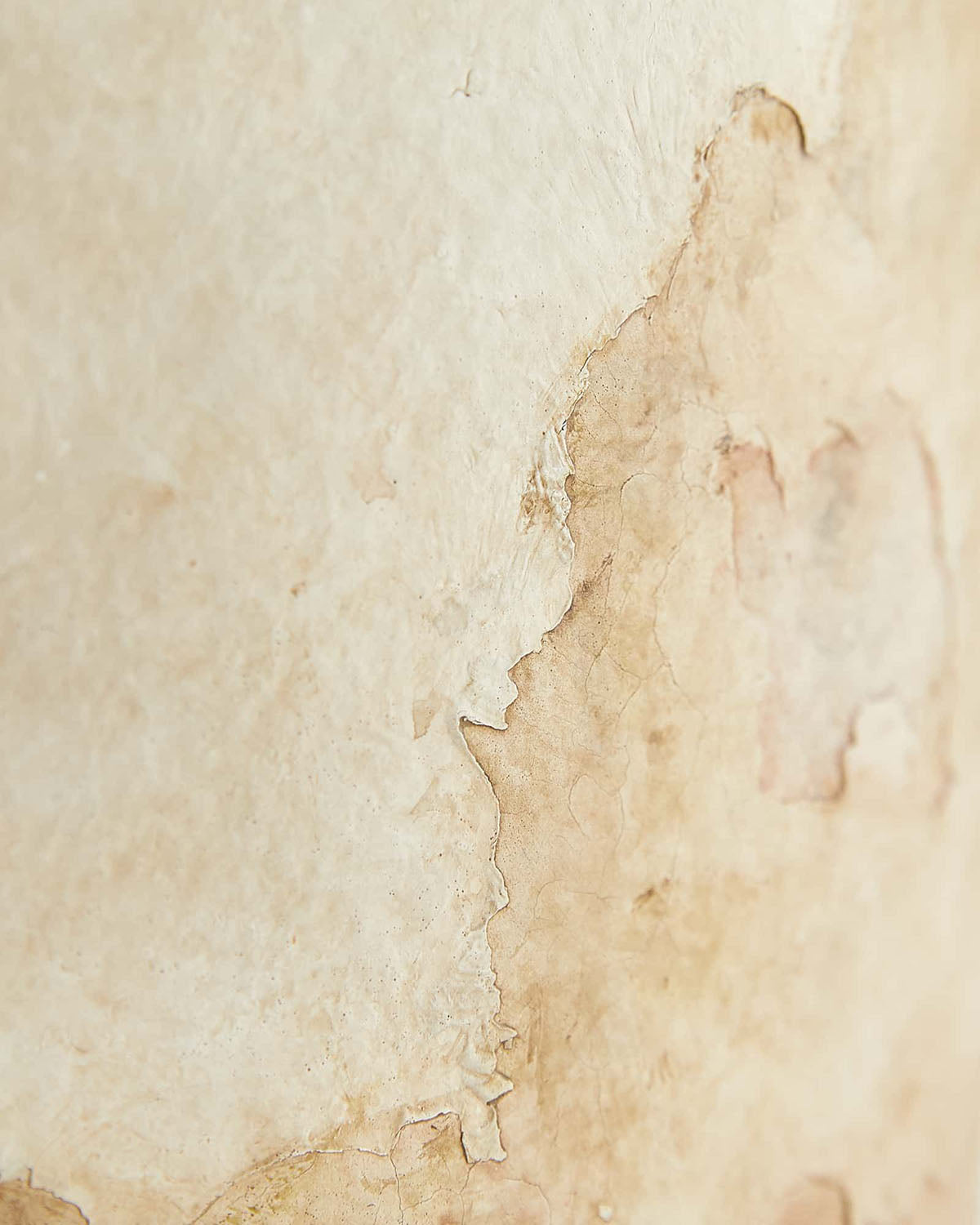 Close-up of a beige wall with peeling paint and stains, revealing a rough, aged texture—an evocative vintage-style backdrop ideal for showcasing the Samala Lamp by McGee & Co.