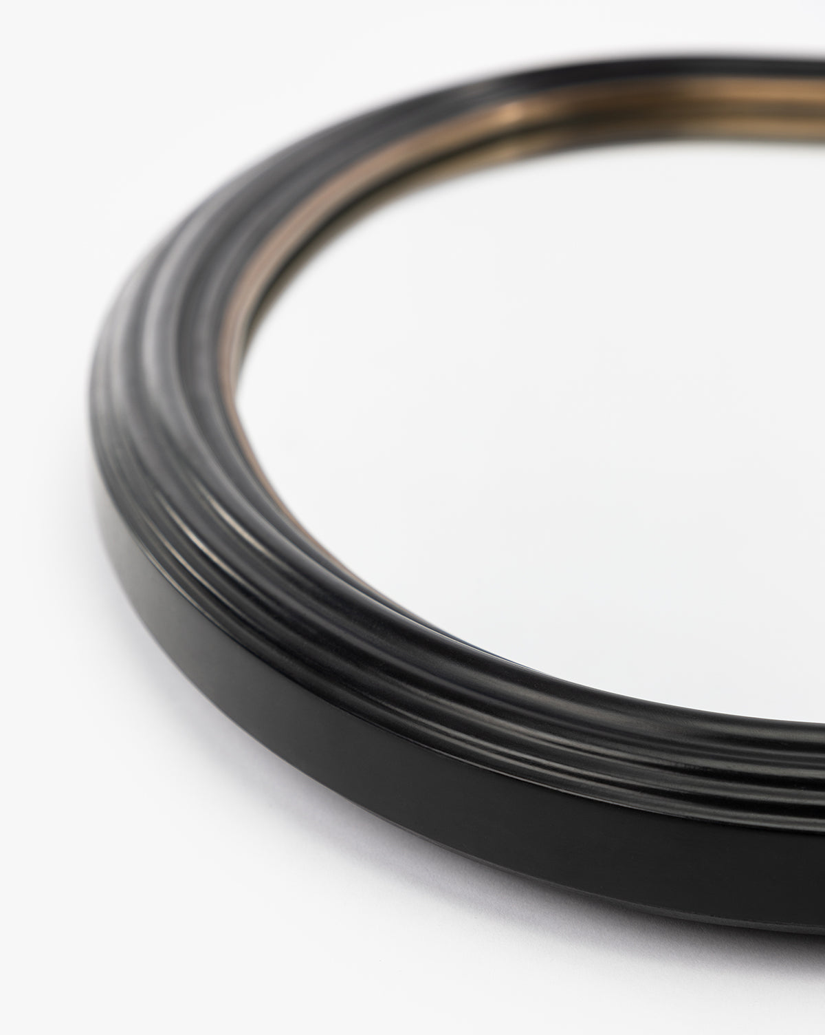 Close-up of the Samuel Wall Mirror, featuring a round black ridged wood frame with a metallic inner edge, displayed on a white surface by McGee & Co.