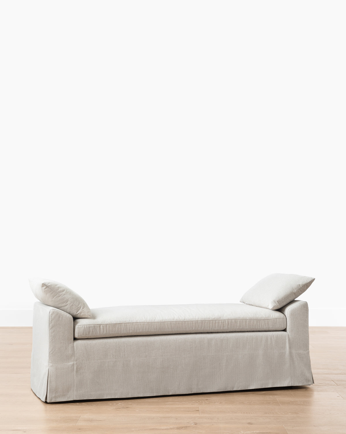 The Scaletta Bench (Ready to Ship) has a modern rectangular design with linen upholstery in light grey and two angled back cushions, set on a light wood floor against a plain white wall, by McGee & Co.