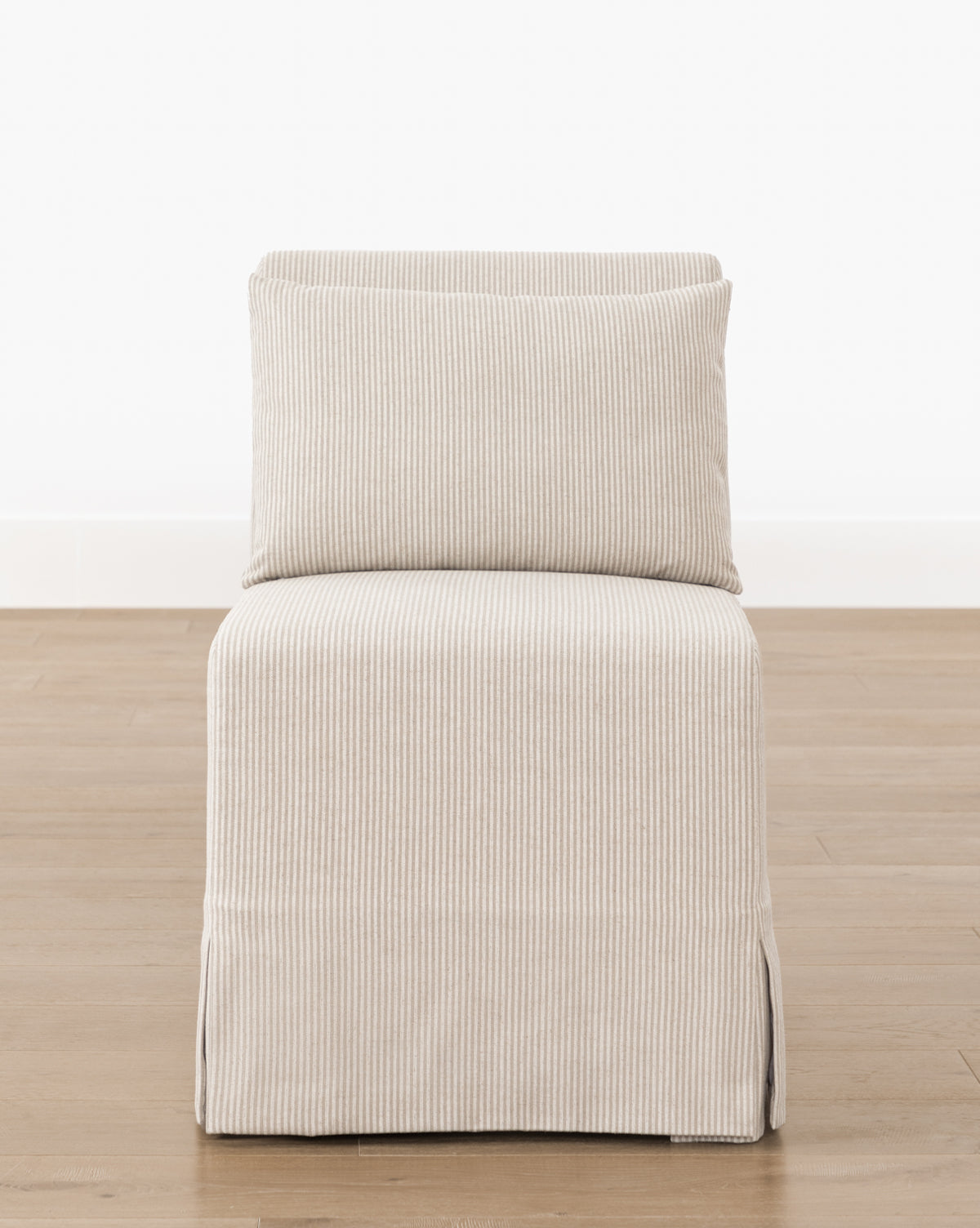 The Scaletta Desk Chair, upholstered in beige fabric with thin vertical stripes and a cushioned seat and matching backrest, stands on a wooden floor against a plain white wall, by McGee & Co.