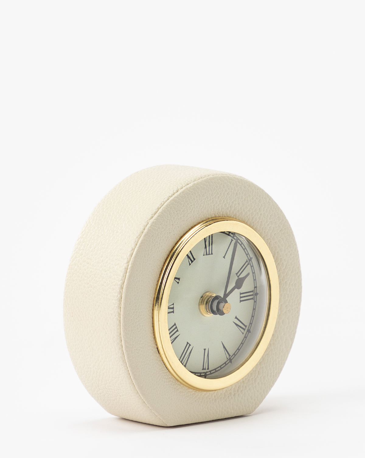 The Shagreen Table Clock features a round, gold-trimmed design with Roman numerals, angled on a white background and encased in light beige cream shagreen leather. The clock displays the time as approximately 1:09.