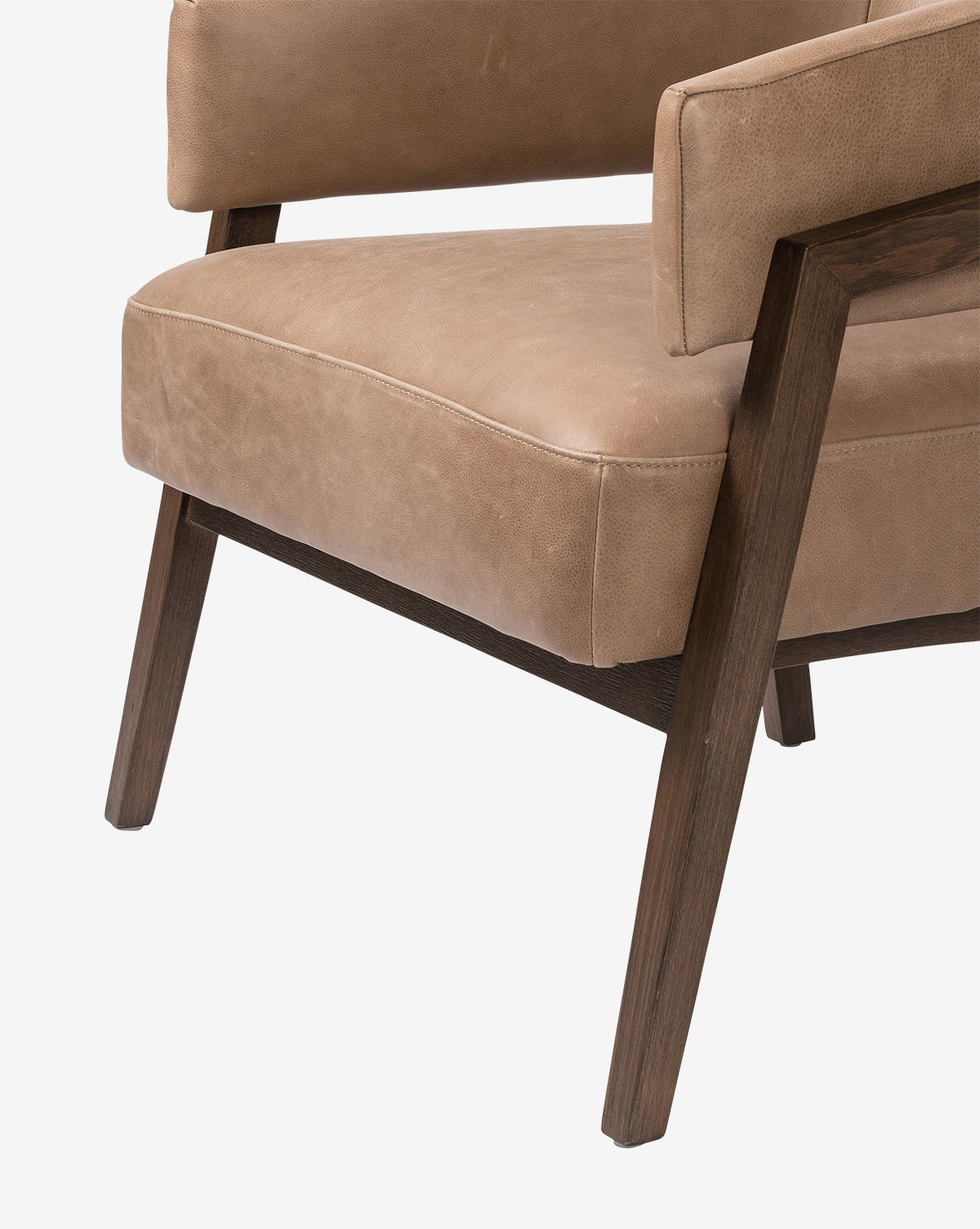 A close-up of the Stanley Lounge Chair, a modern lounge chair featuring light brown leather upholstery and angled wooden legs, highlights the seat, armrest, and part of the backrest against a white background by McGee & Co.