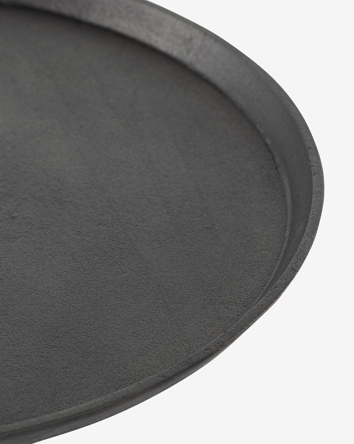 Close-up of the edge of the round, black Sheba Side Table by Four Hands, shown on a white background. Its textured matte surface evokes the look of aged grey iron, McGee & Co.