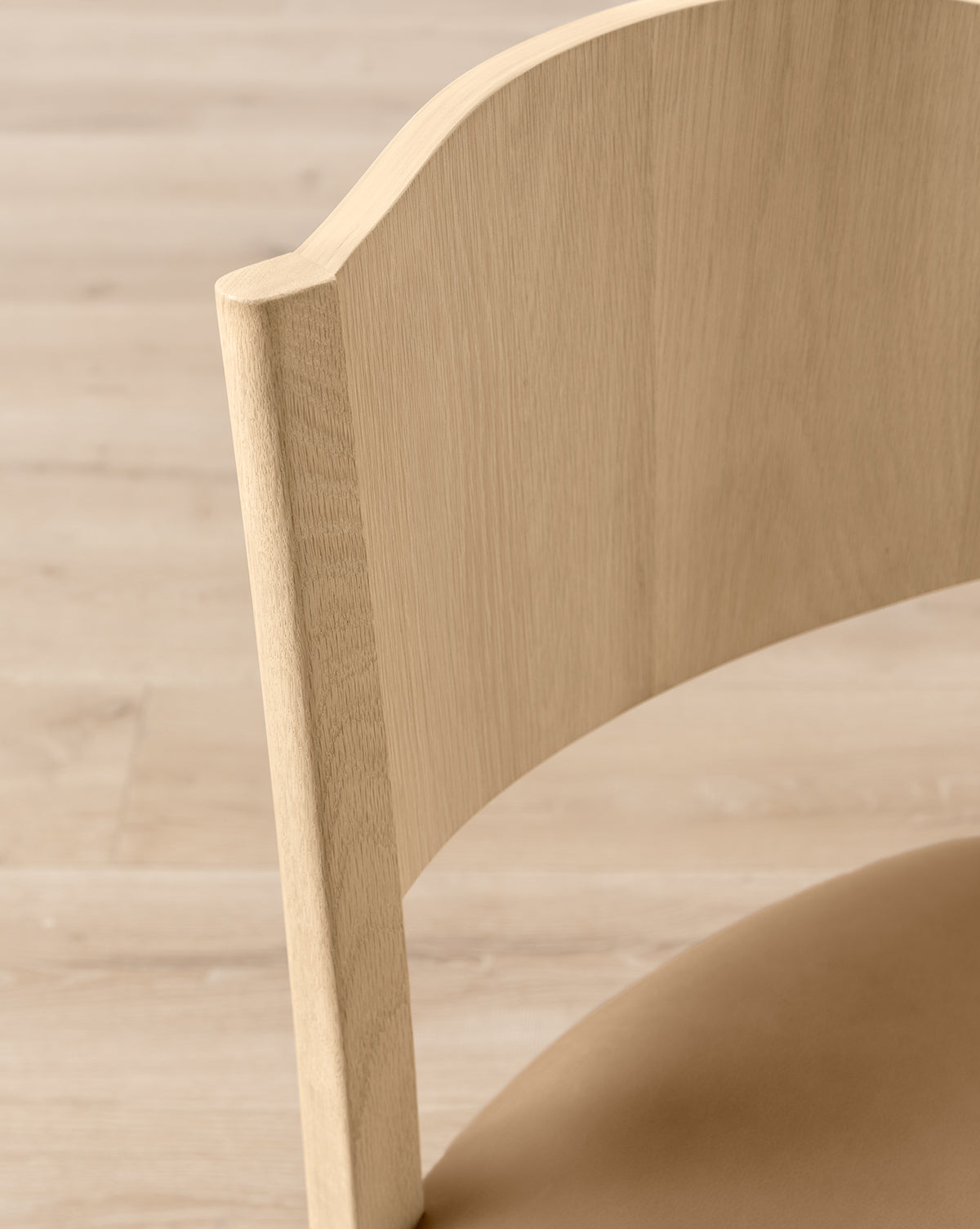 A close-up of the Shepherd Dining Chair showcases its white oak frame, curved backrest, and seat, set against a matching light wood floor, by McGee & Co.