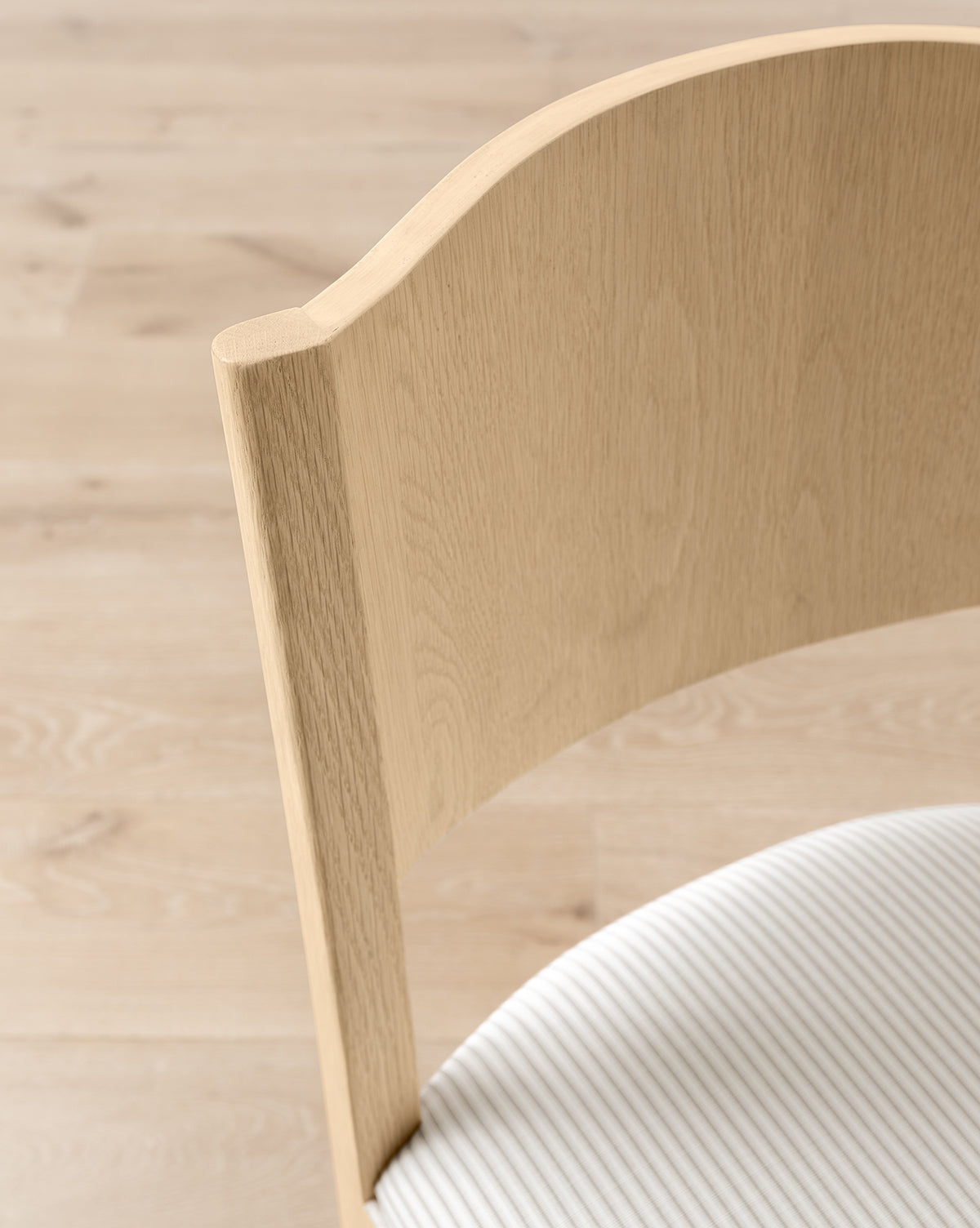 Close-up of the Shepherd Dining Chair with a white oak frame, curved backrest, and ribbed white upholstered seat cushion, shown on a light wood floor, by McGee & Co.
