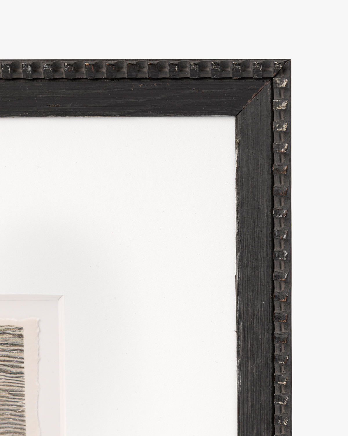 Close-up of the top right corner of a black Shoals Engraving frame with a textured, decorative edge, showing part of a matted seascape sketch against a white background, by McGee & Co.