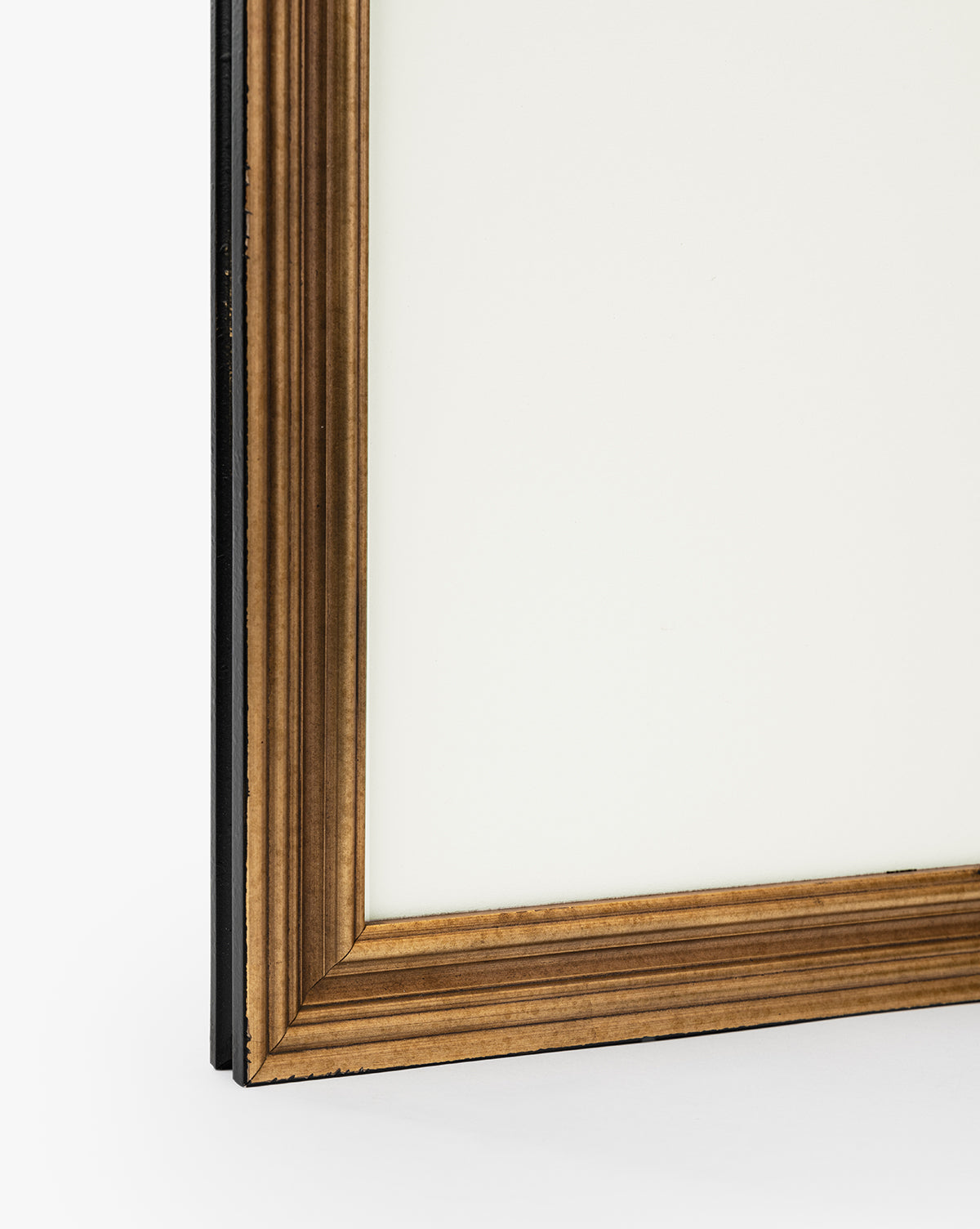 Close-up of the bottom left corner of a picture frame with a gold-toned, ridged border and white background—ideal for displaying the Shoreline Rocks print against a plain white surface, by McGee & Co.