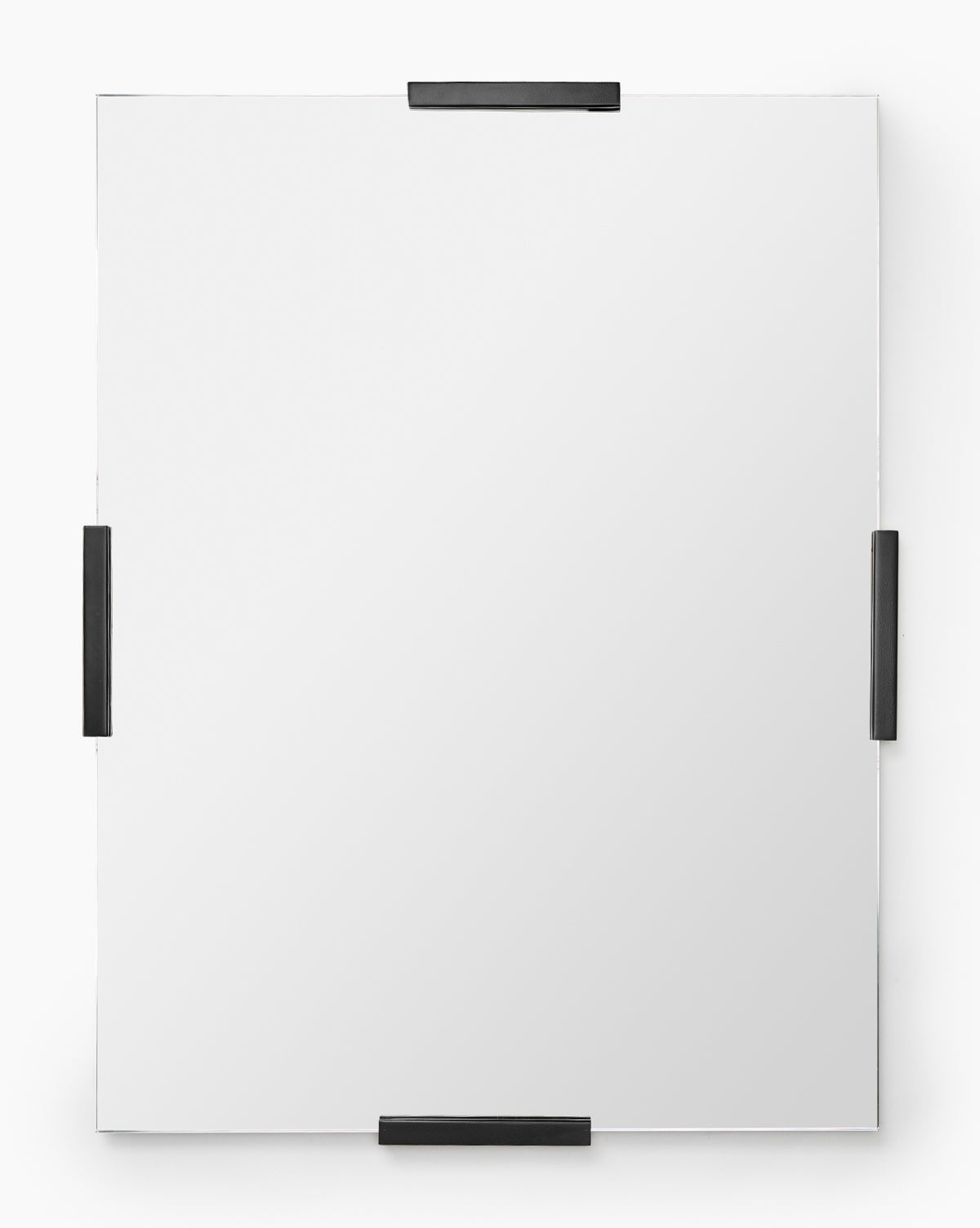 The Slade Mirror is a modern, rectangular frameless mirror secured with four black metal clips on each side, creating a subtle metallic accent against a plain white background, by McGee & Co.
