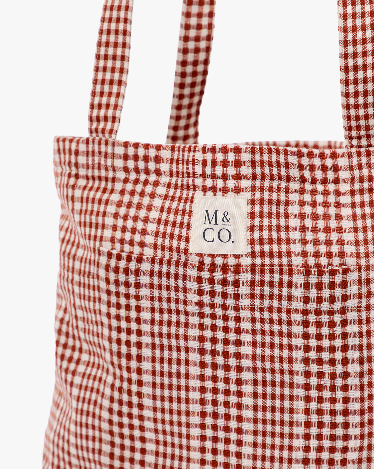 Close-up of the Spencer Tote Bag, featuring red and white gingham fabric and two handles. A small white label near the top displays "M & CO." in black letters, by McGee & Co.