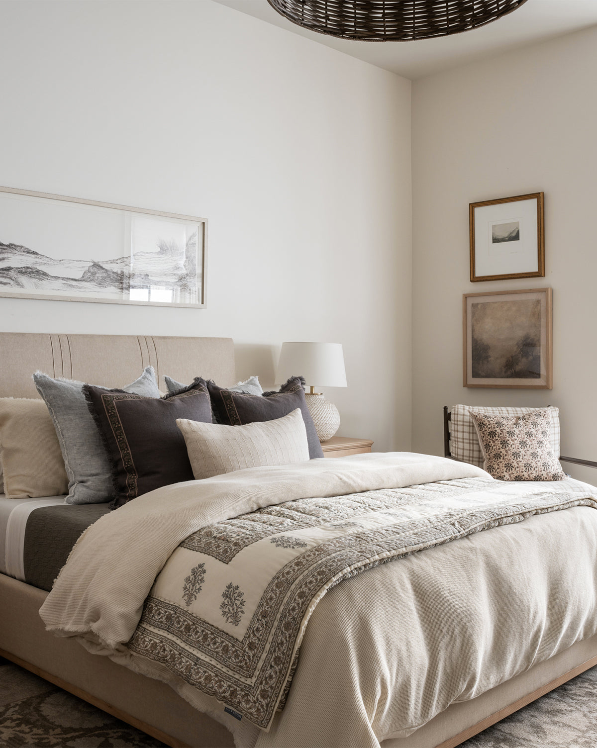 A cozy bedroom with a neatly made bed, plush neutral bedding, a bedside lamp, and Window to the Mountains—gallery-quality framed mountain landscape art—displayed on the cream-colored walls.