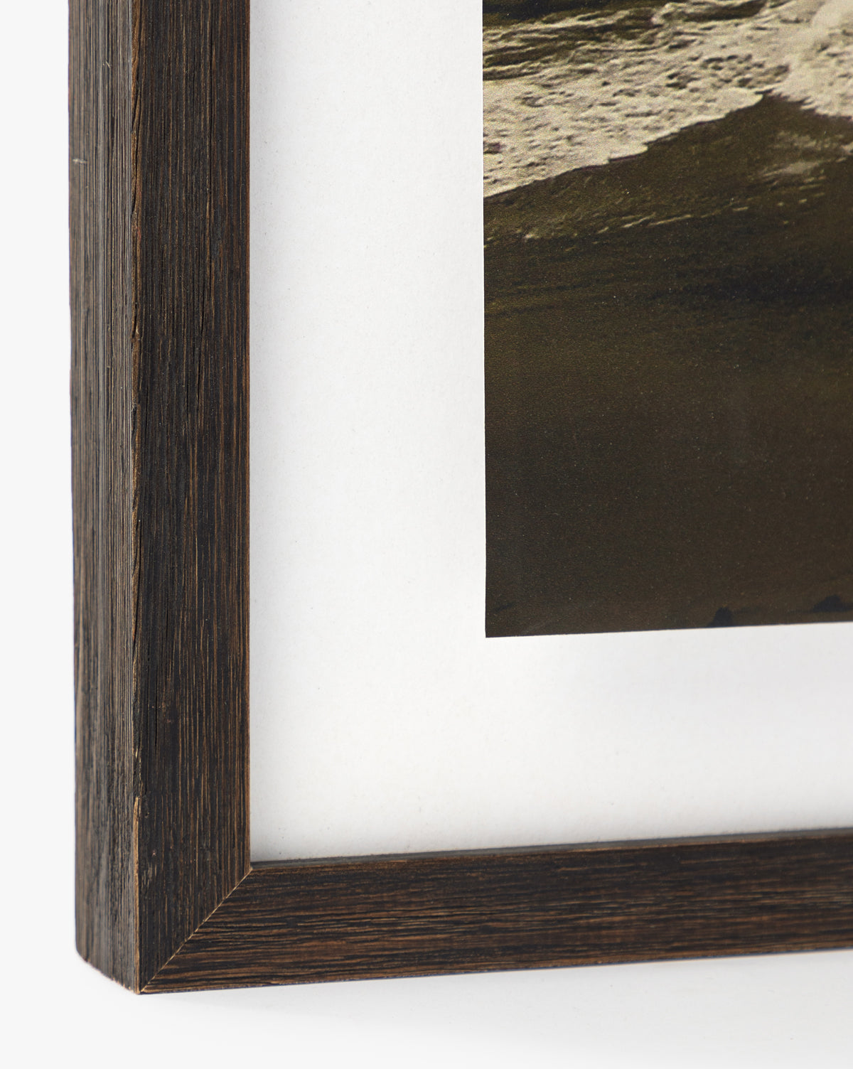 Close-up of a dark walnut wood frame with white mat, showcasing part of the Sunday Fog giclee print—featuring waves along the edge of a beach with dark sand.