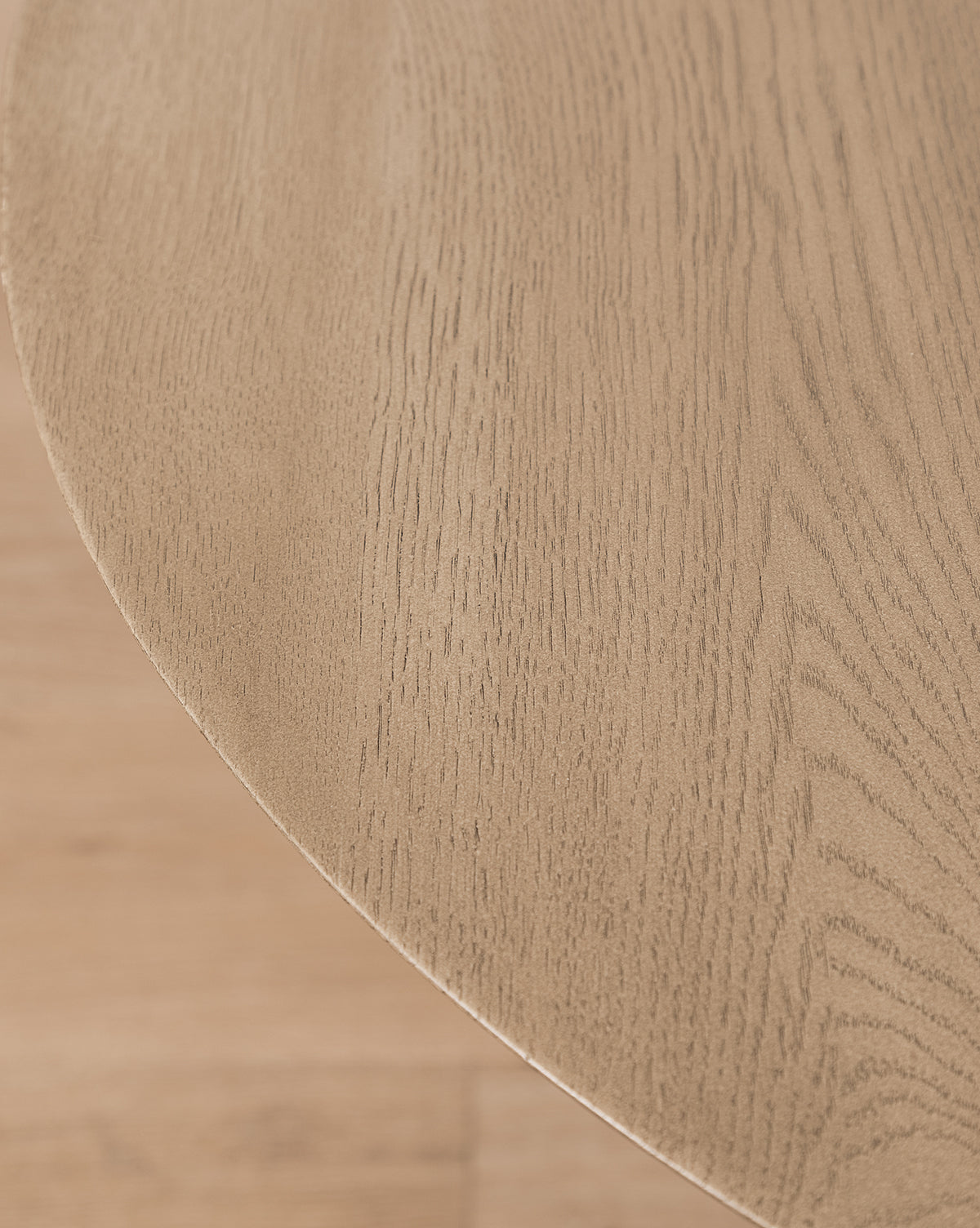 A close-up of the Tavin Side Table shows its smooth solid white oak surface and natural wood grain. The modern table’s curved edge appears in the upper left corner of the image.