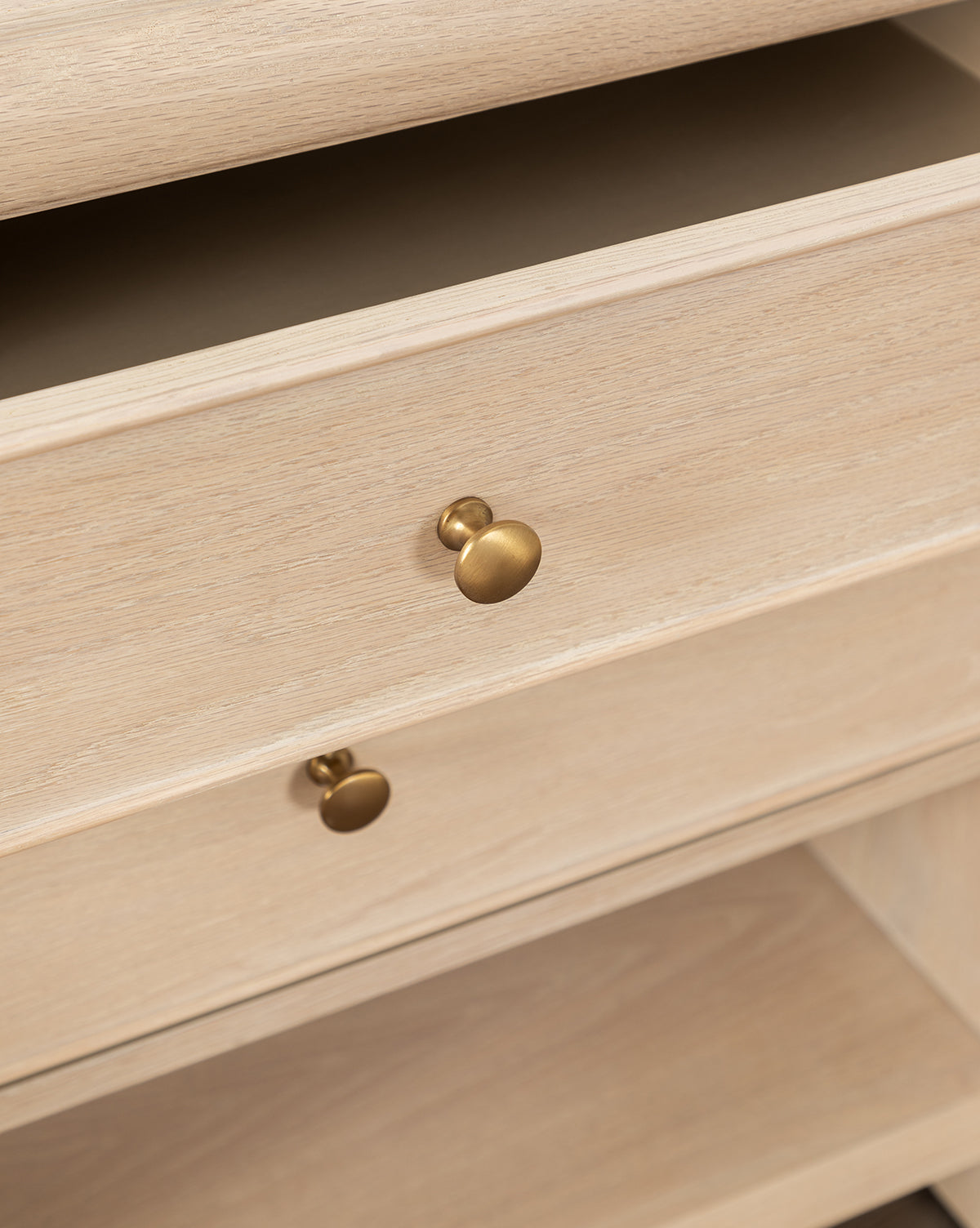 Close-up of the Tellerbeck Nightstand in bleached oak, featuring round gold-tone knobs, an open lower shelf, and a partially open drawer that reveals the interior—ideal for adding refined style to your bedroom, by McGee & Co.