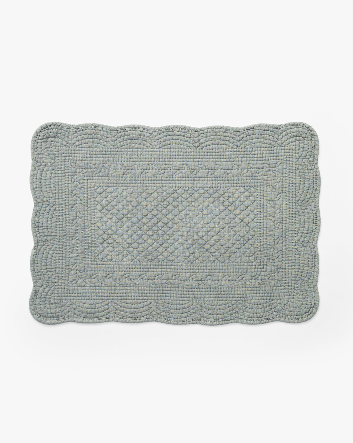 The Thorin Quilted Placemat is a rectangular, light blue placemat with scalloped edges and a textured pattern—perfect for adding elegance to any table, by McGee & Co. Shown on a white background.
