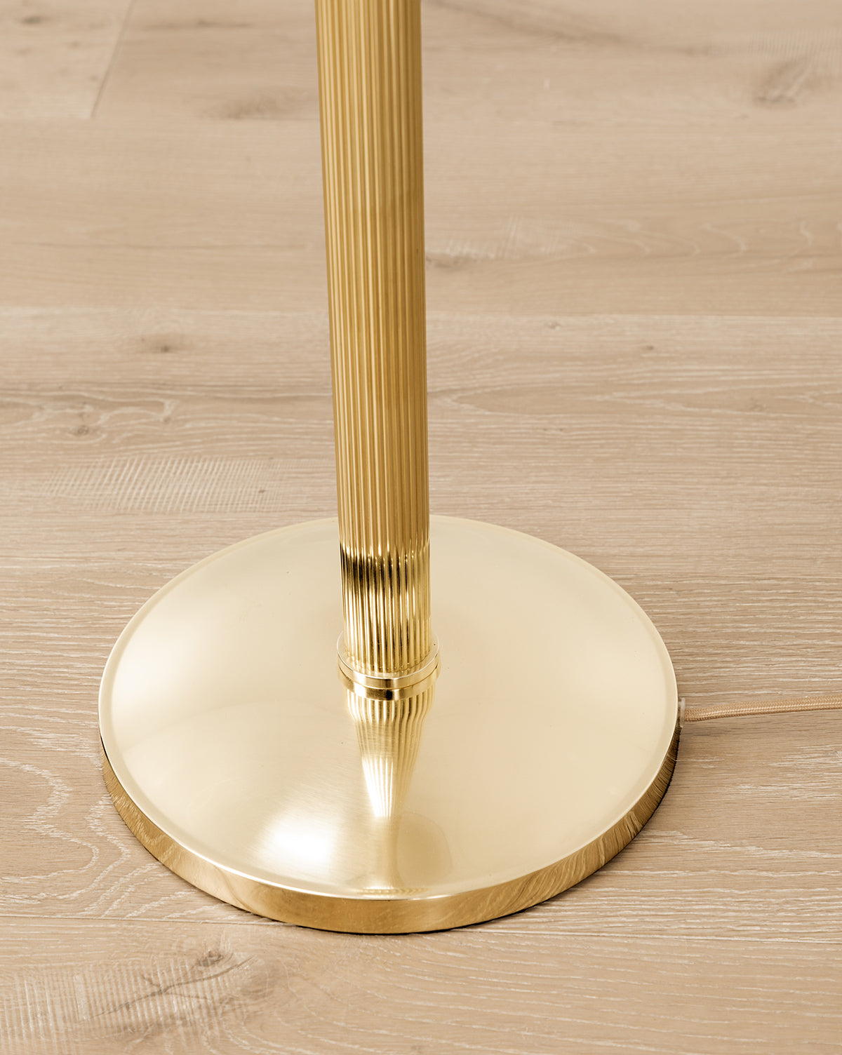 A close-up of the Townes Floor Lamp’s shiny, reeded brass base with a ribbed pole, standing on a light wood floor, by McGee & Co.