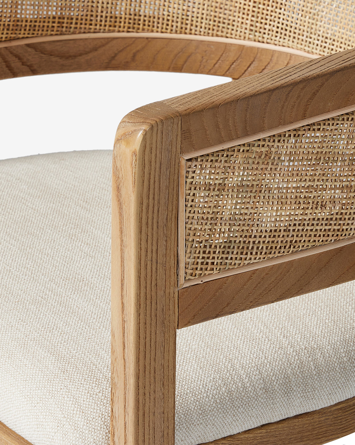 Close-up of the Valissa Dining Armchair, showcasing its light wooden frame, woven cane seatback and armrests, plus an off-white cushioned seat. Set against a white background to highlight its modern design by McGee & Co.