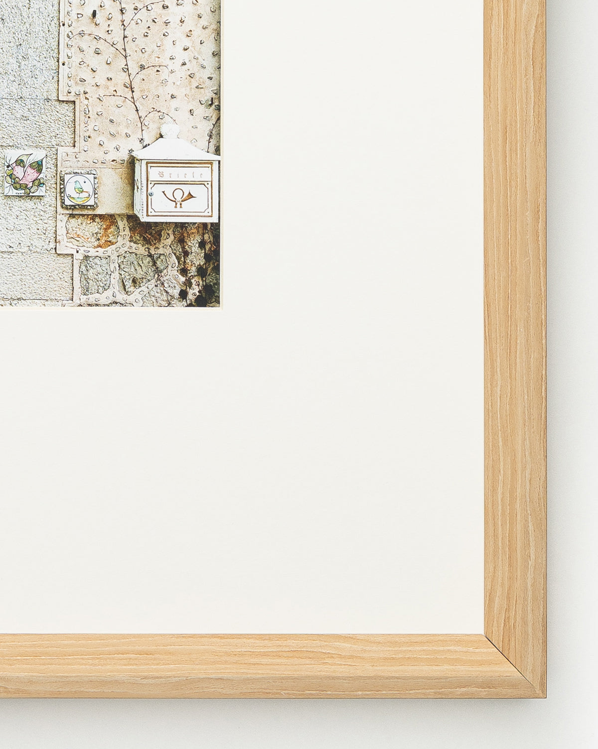 A close-up of the Valldemossa framed photo displays part of a building exterior with a mailbox and doorbell. The light wood frame highlights its natural woodgrain, and the wide white mat mostly surrounds the image.