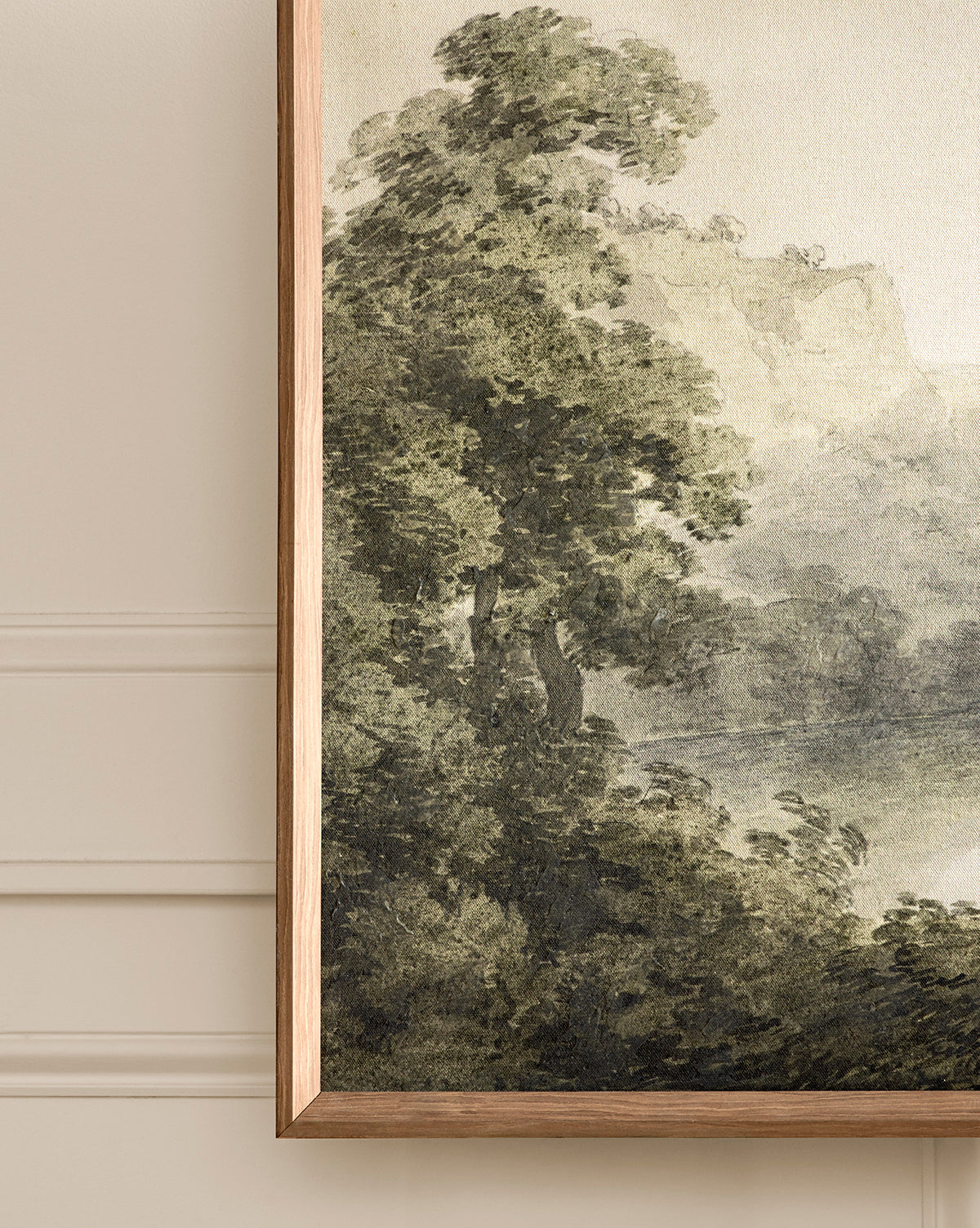 A close-up of the Verde Landscape giclee print, featuring tall leafy trees in muted greens with cliffs and a soft sky, framed and hanging on a beige wall with decorative molding.
