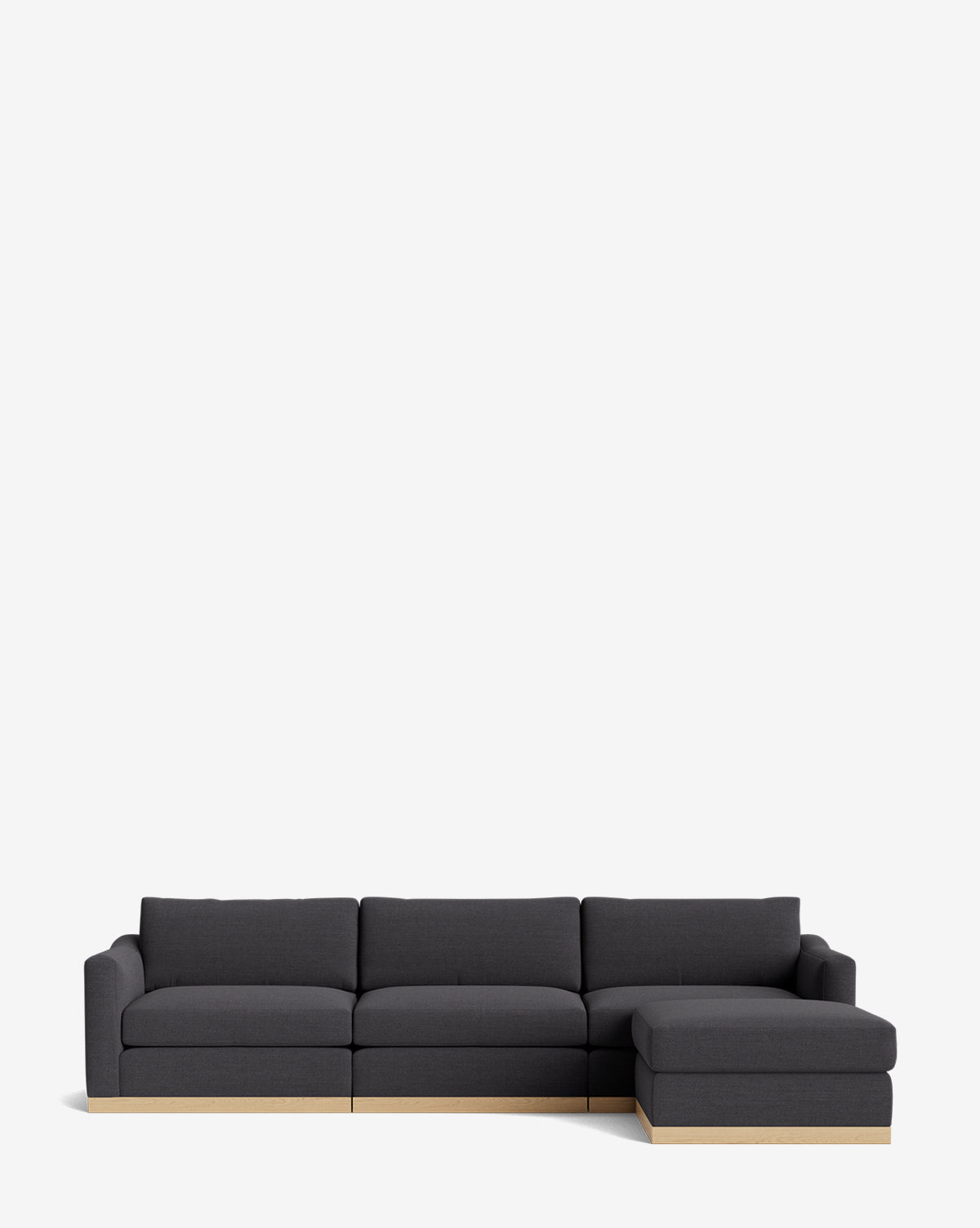 The Vernon Modular Sofa with Ottoman 121 is a modern dark gray fabric sectional with three seat cushions, a right-side chaise lounge, an ottoman, and light wood trim at the base, shown against a plain white background by McGee & Co.
