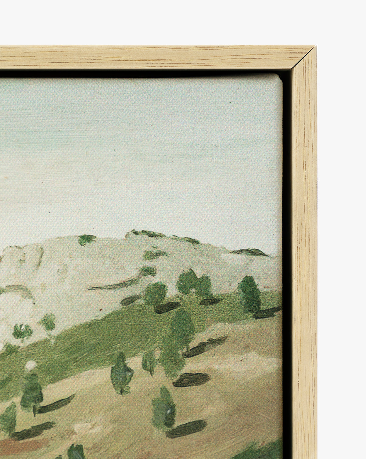 A close-up of View of the Town, a framed painting depicting a hilly landscape with scattered trees beneath a pale sky. The oak frame is visible along the right and top edges, by McGee & Co.