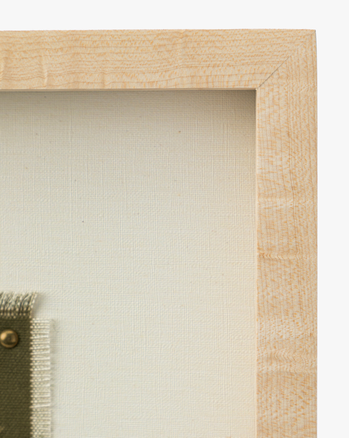 A close-up of the top right corner of a light oak frame displays a museum-quality canvas and green fabric secured by a brass pin, from the series Viewpoint by Britney Schulz, by McGee & Co.