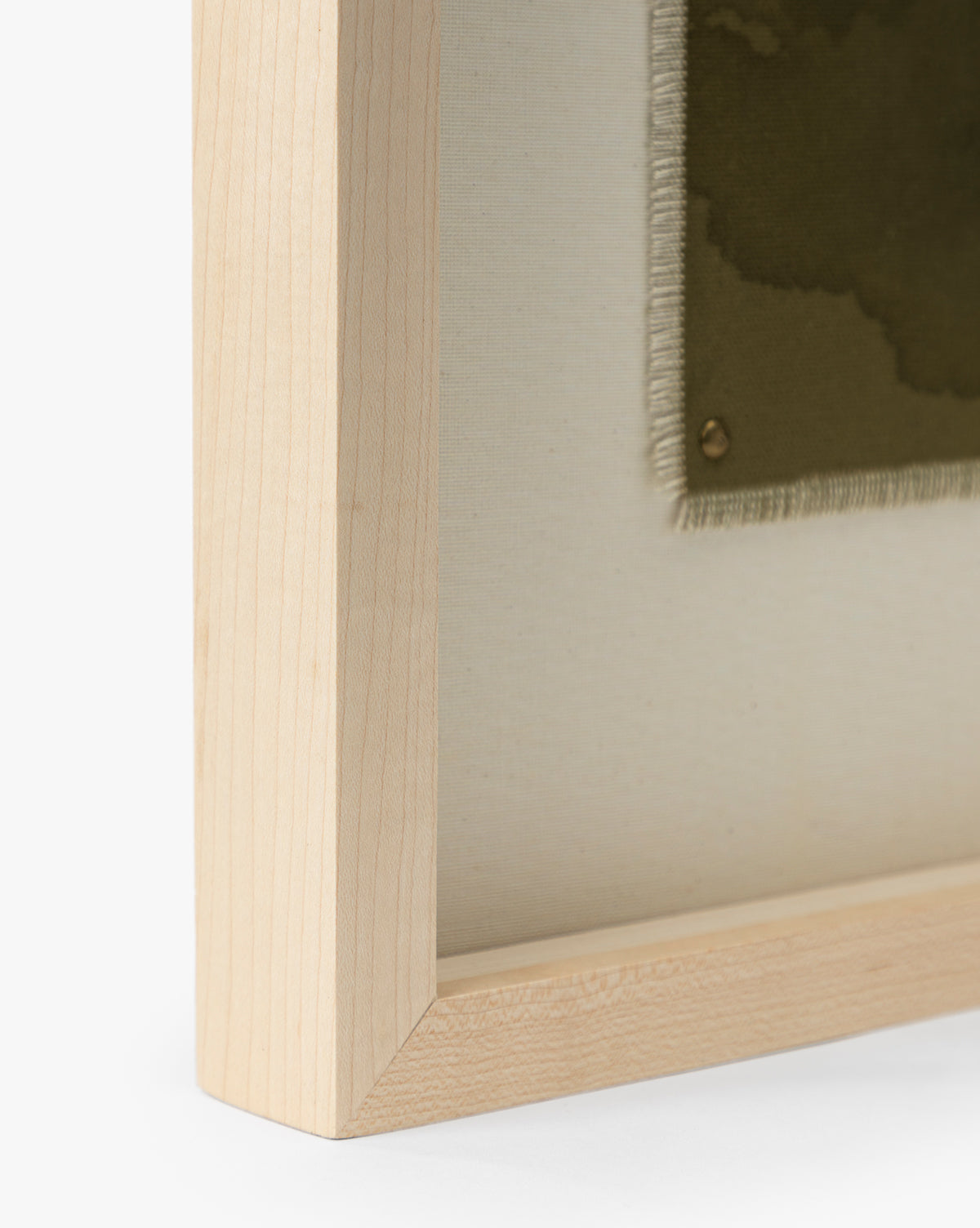 Close-up of a light oak frame corner with a stretched museum-quality canvas from Viewpoint by Britney Schulz. The canvas displays a green fabric swatch secured by a brass tack, its frayed edges partially visible by McGee & Co.