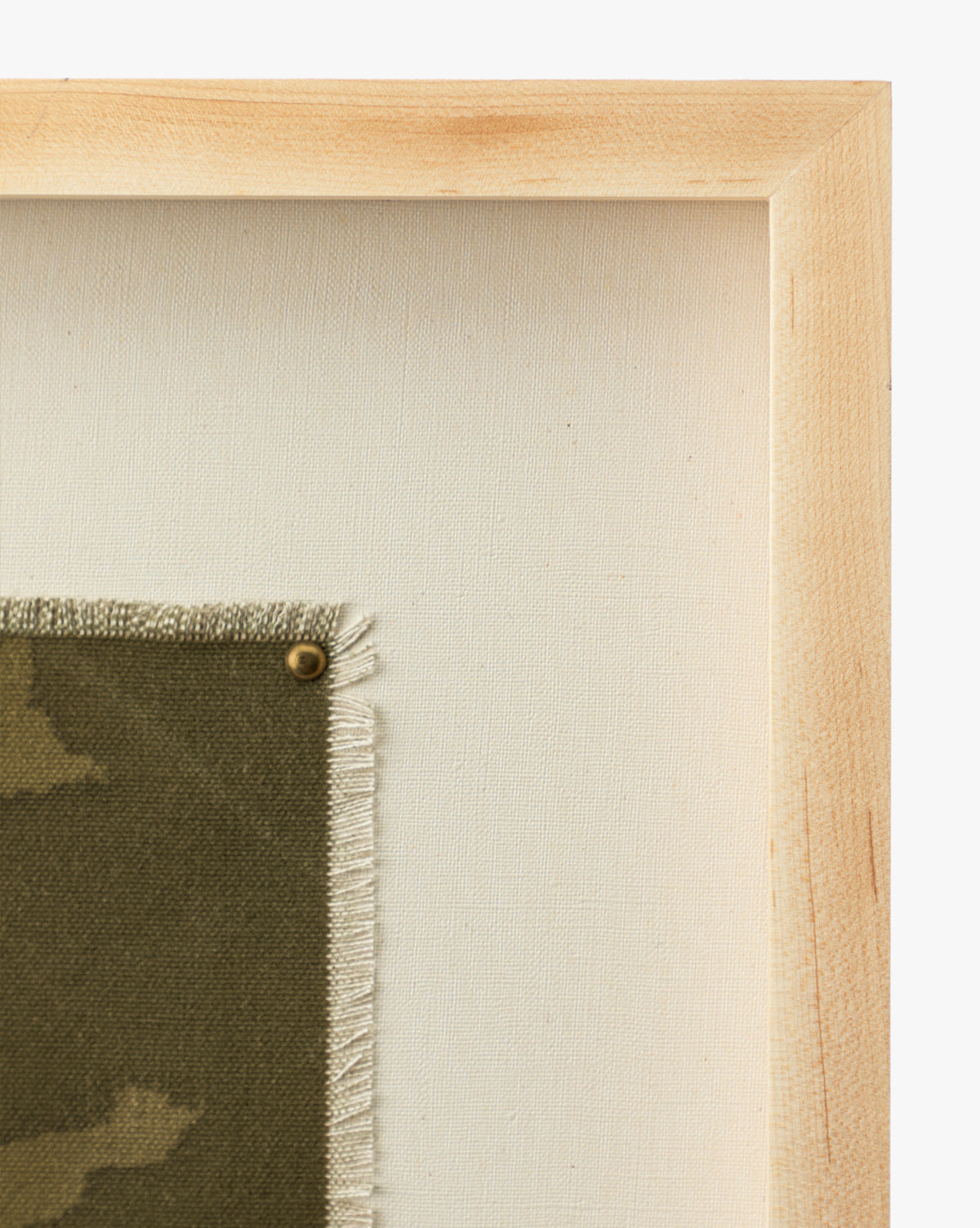 Close-up of the light oak frame for Viewpoint by Britney Schulz, showcasing museum-quality canvas with green patterned fabric, frayed edges, and a brass tack, all set against a plain off-white background by McGee & Co.