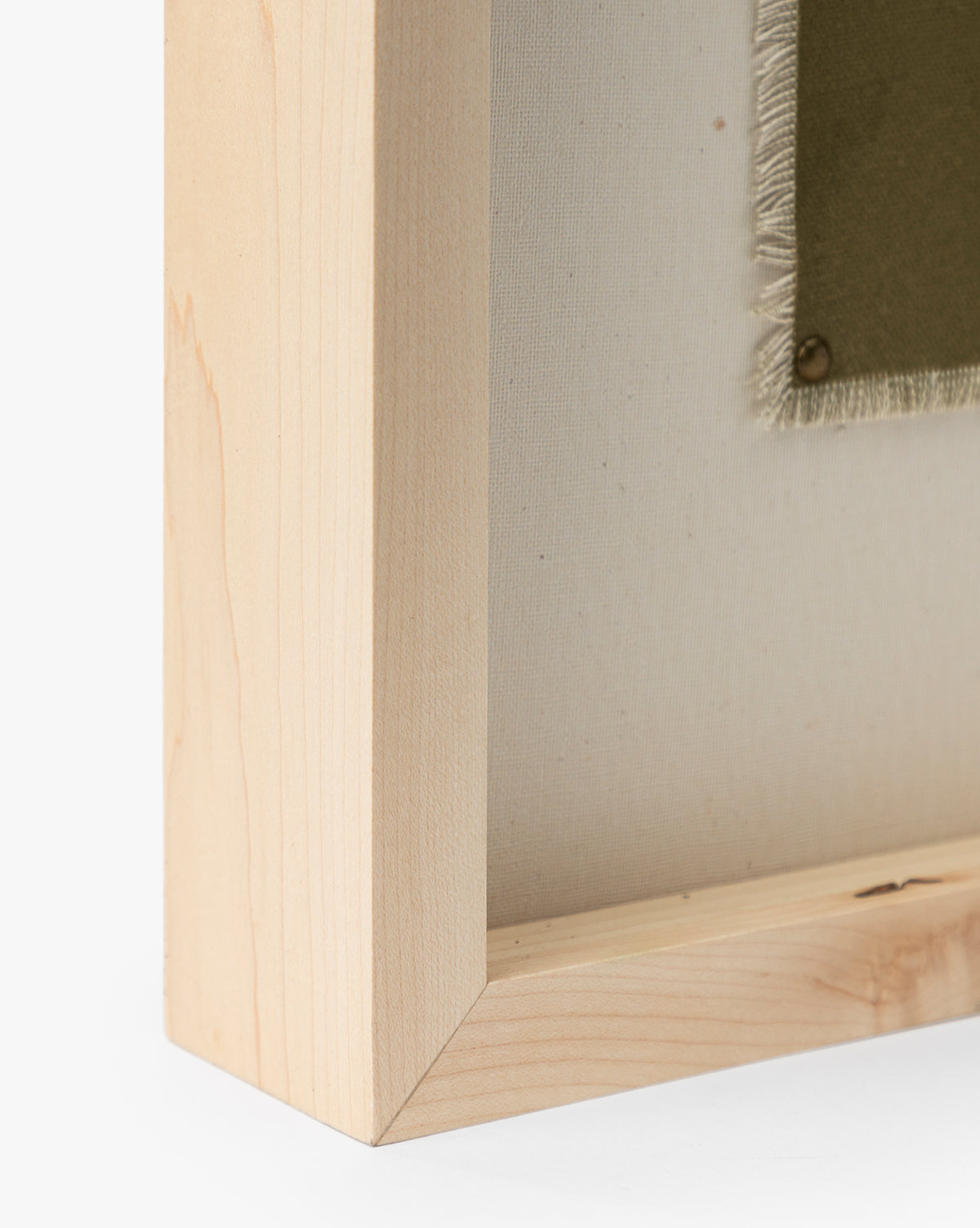 Close-up of the corner of a light oak frame for Viewpoint by Britney Schulz, showing the museum-quality canvas edge and olive green fabric secured with a brass tack, by McGee & Co.
