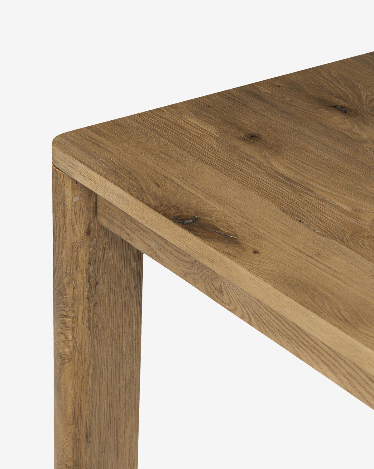 Close-up of the Wagner Extension Dining Table’s corner, highlighting its sturdy oak construction, natural finish, and elegant wood grain. The tabletop and one leg are featured against a white background by McGee & Co.