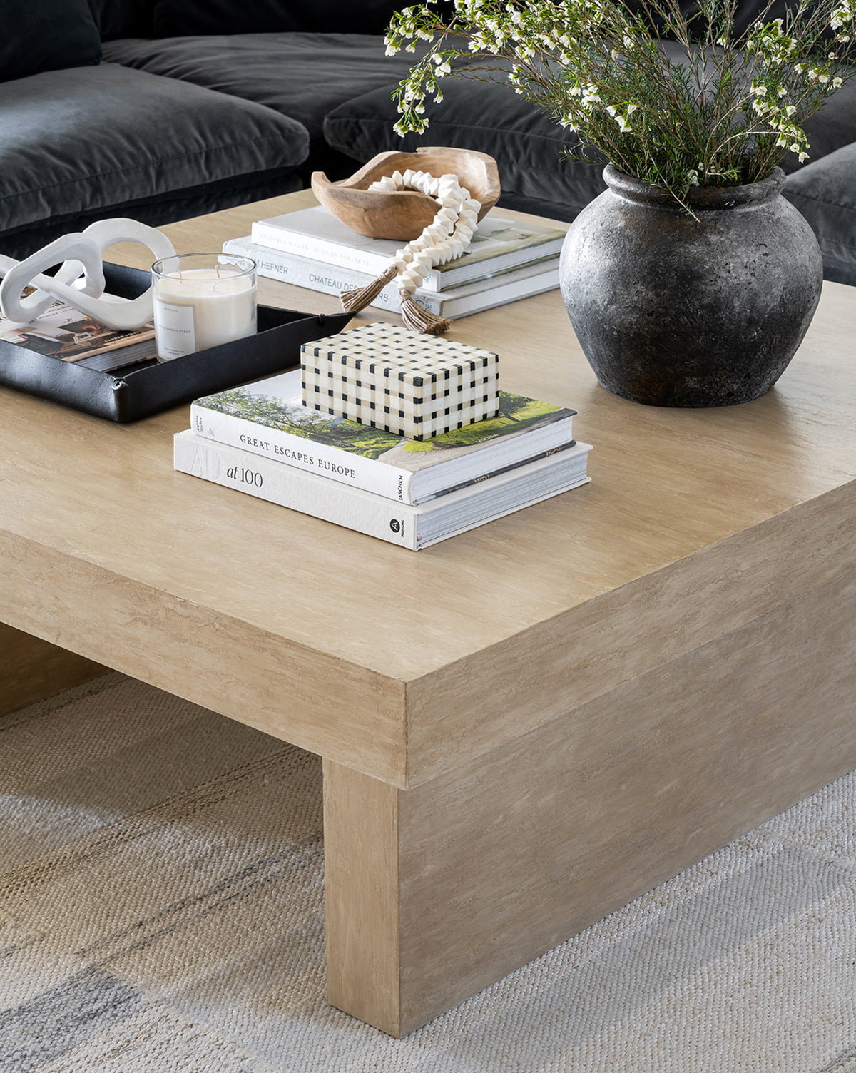 An Aged Terracotta Jar, stacked books, bowl, beaded ornament, and candles sit on a wooden coffee table atop a textured rug—perfect for fans of modern living rooms and textured home decor.