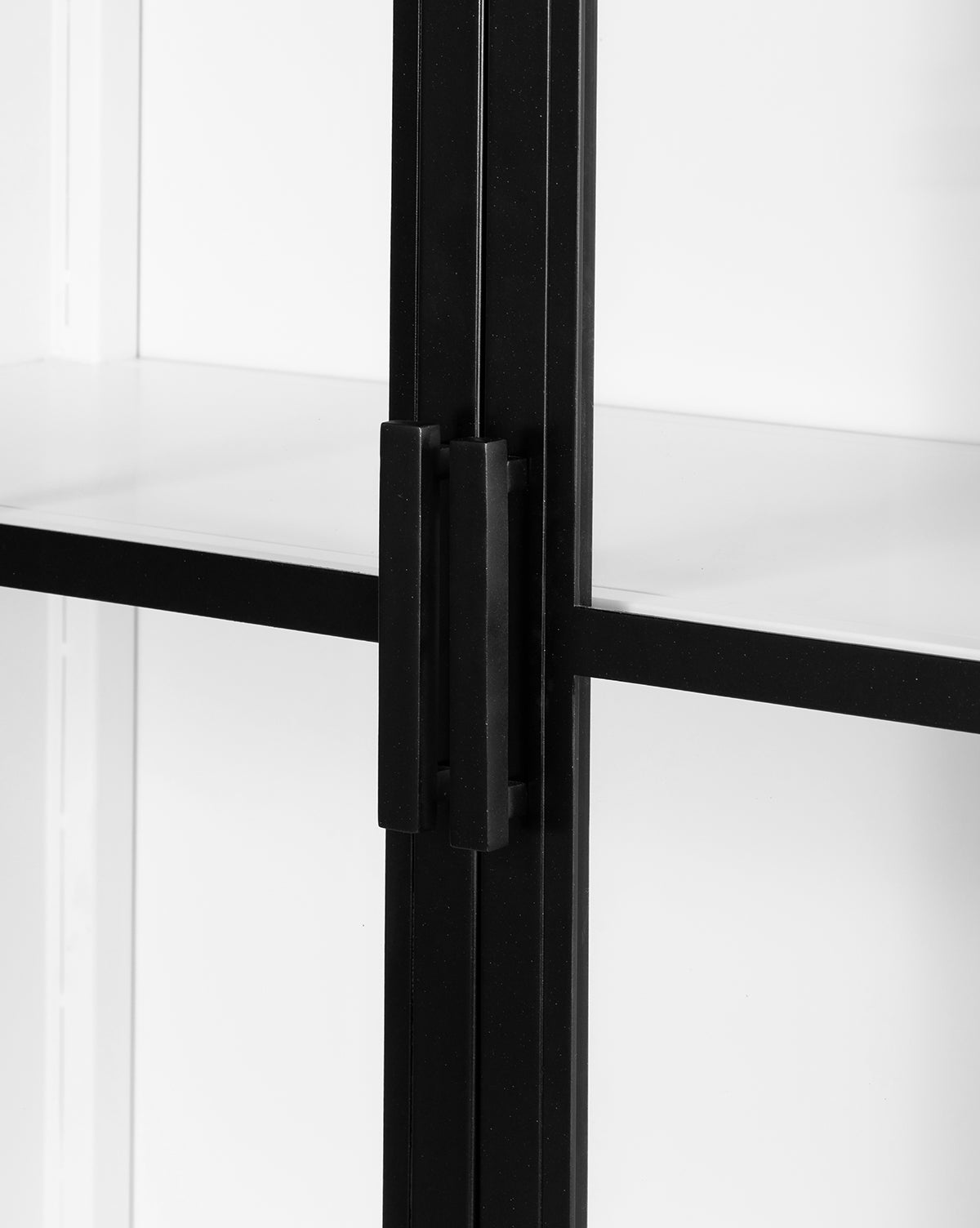 Close-up of the black metal handle on the Waylon Cabinet’s tempered glass door, with a black iron frame and white interior shelves, showcasing its modern, minimal design, by McGee & Co.