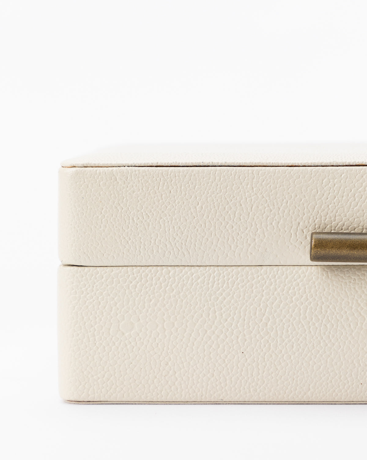 Close-up of the Cream Shagreen Box’s side, featuring its metallic gold handle. Only a portion of this decorative storage box and its elegant handle are visible against a white background.