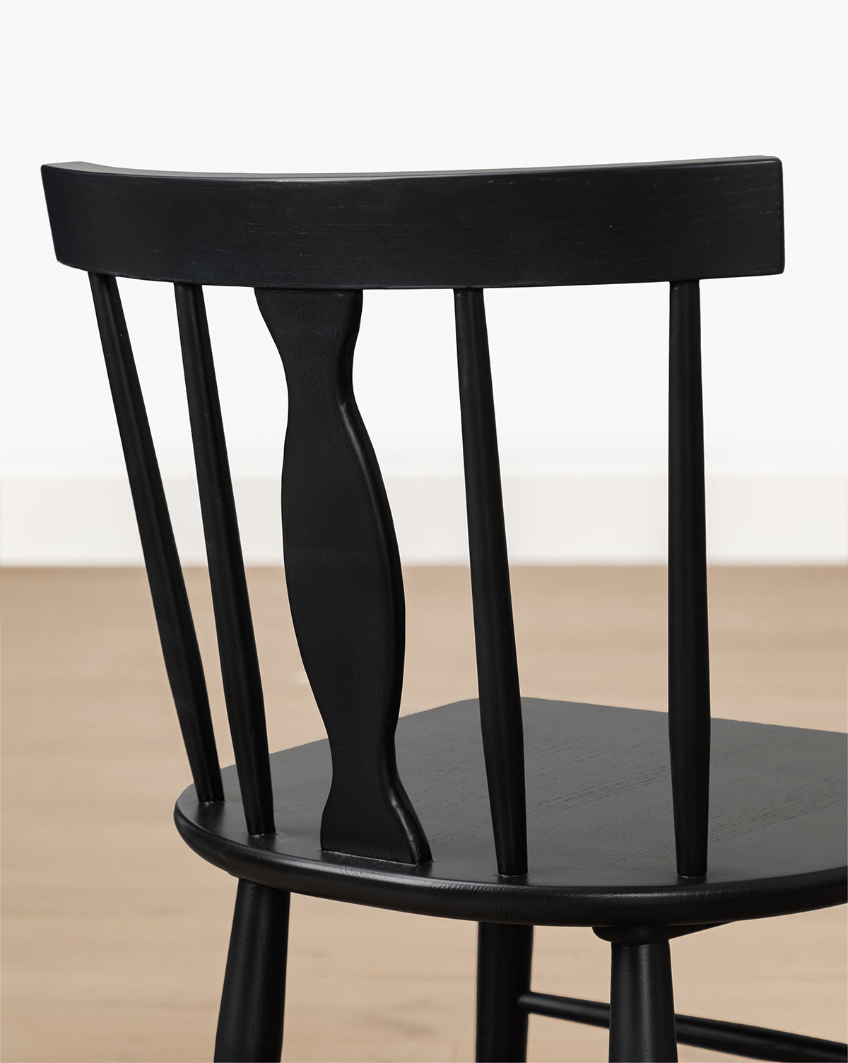 The Whittaker Chair, made from solid oak, features a curved backrest and vertical slats. Set on a light wood floor against a white wall, it adds timeless style to your dining space, by McGee & Co.