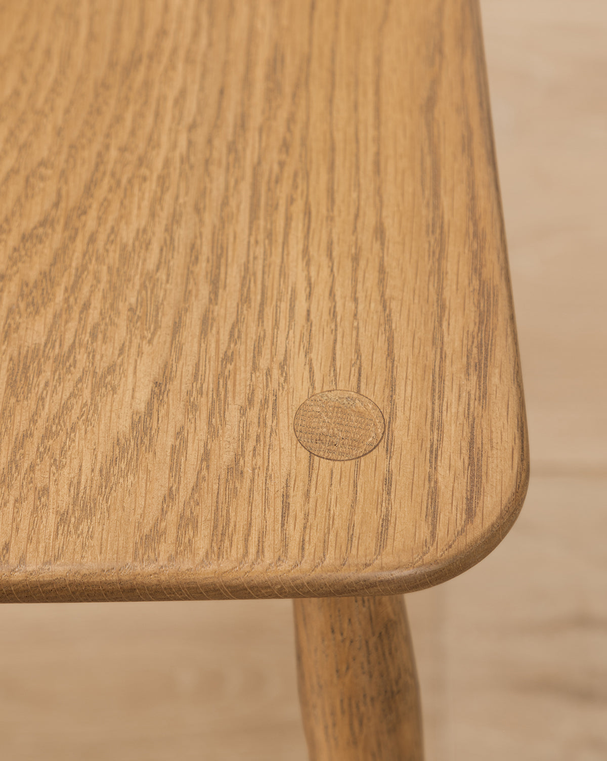 Close-up of a solid oak table corner with a round wooden plug highlights the natural grain and smooth finish—an ideal accent for any dining space, perfectly pairing with the Whittaker Chair, by McGee & Co.