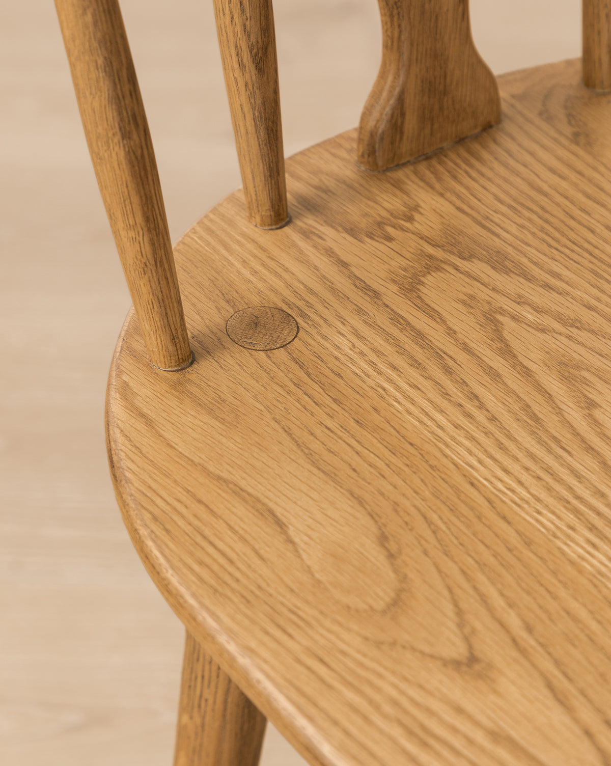 Close-up of the Whittaker Chair seat in solid oak, showcasing its natural wood grain, smooth finish, and vertical back spindles. A small round plug is visible on the seat—an elegant touch for any dining area, by McGee & Co.