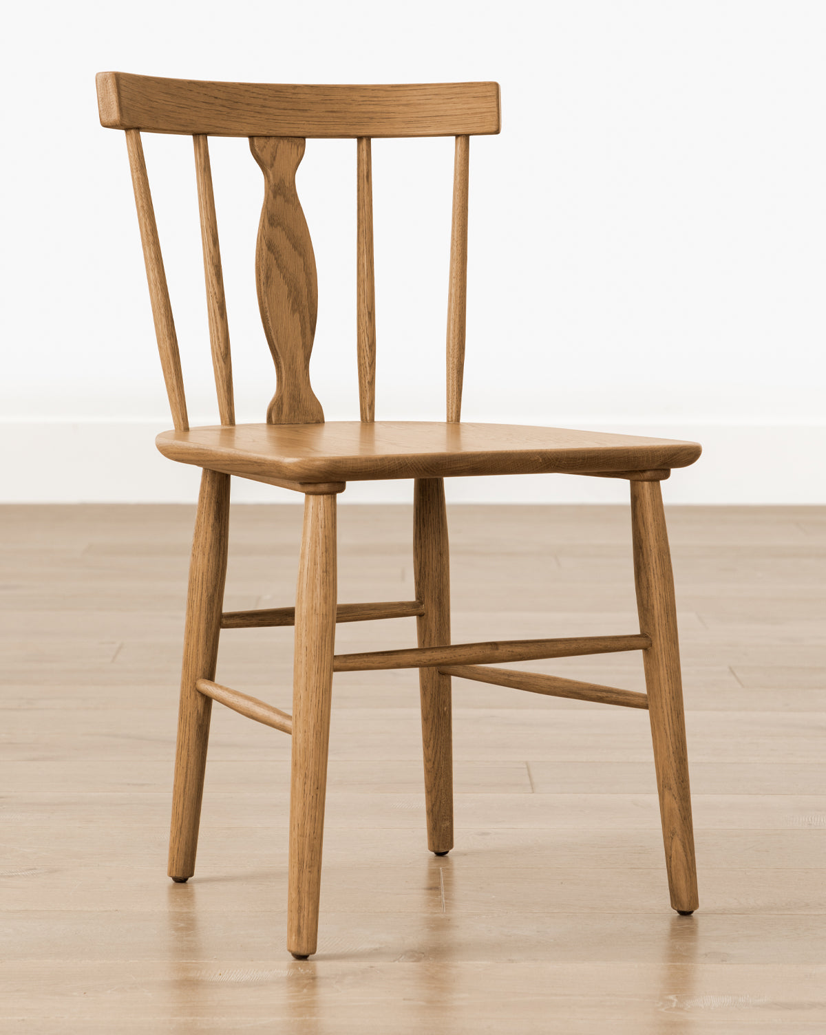 The Whittaker Chair is a solid oak dining chair with a curved backrest, three vertical slats (one carved and wider), a flat seat, and four straight legs—an ideal addition to any dining space, by McGee & Co.