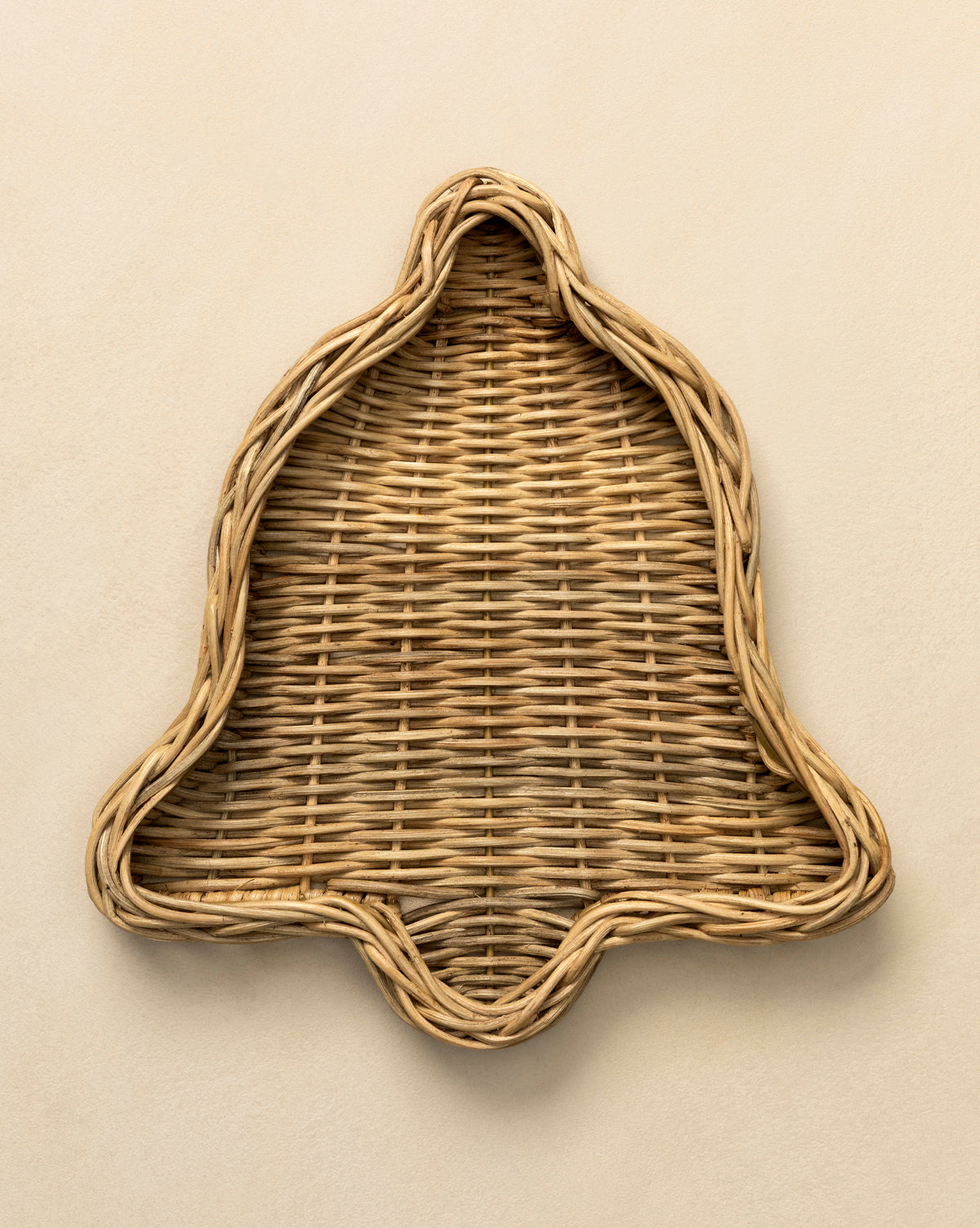 The Wicker Bell Tray, handwoven in a festive bell shape and ideal for holiday entertaining, is displayed on a light beige surface, by McGee & Co.