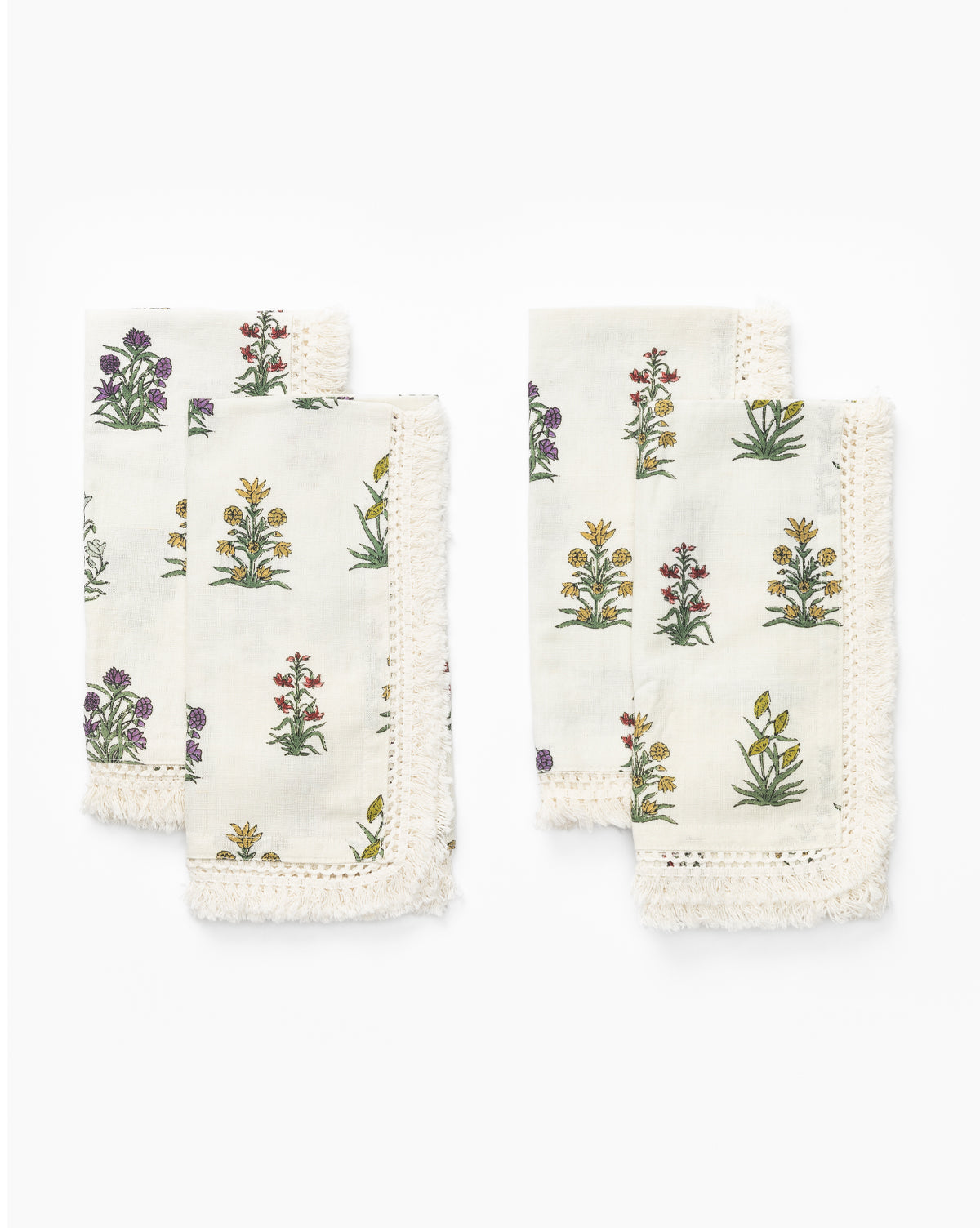 A set of four Wilkie Floral Napkins, crafted from soft cotton with colorful floral block-print-inspired designs and fringed edges, are arranged in two stacks on a white background by McGee & Co.