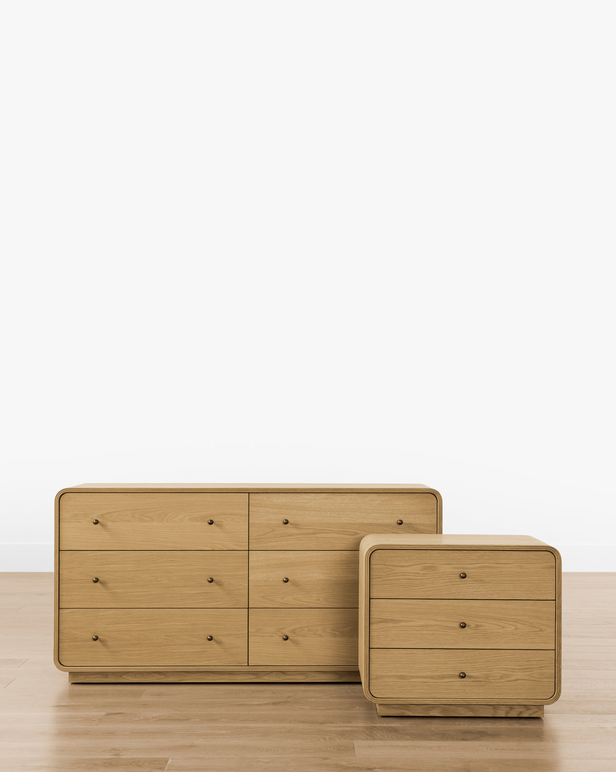 Two light wood dressers with rounded edges stand side by side on a wooden floor against a plain white background. The larger has six drawers, while the smaller is the Wilkins Oak Nightstand with three drawers—ideal for modern bedrooms, by McGee & Co.