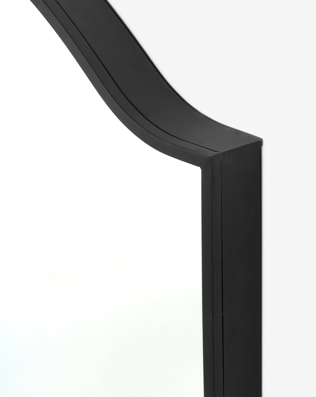 Close-up of the Willson Wall Mirrors upper corner, showcasing its sleek black iron frame, arched design, and rectangular shape—a stylish alternative to classic square mirrors, by McGee & Co.