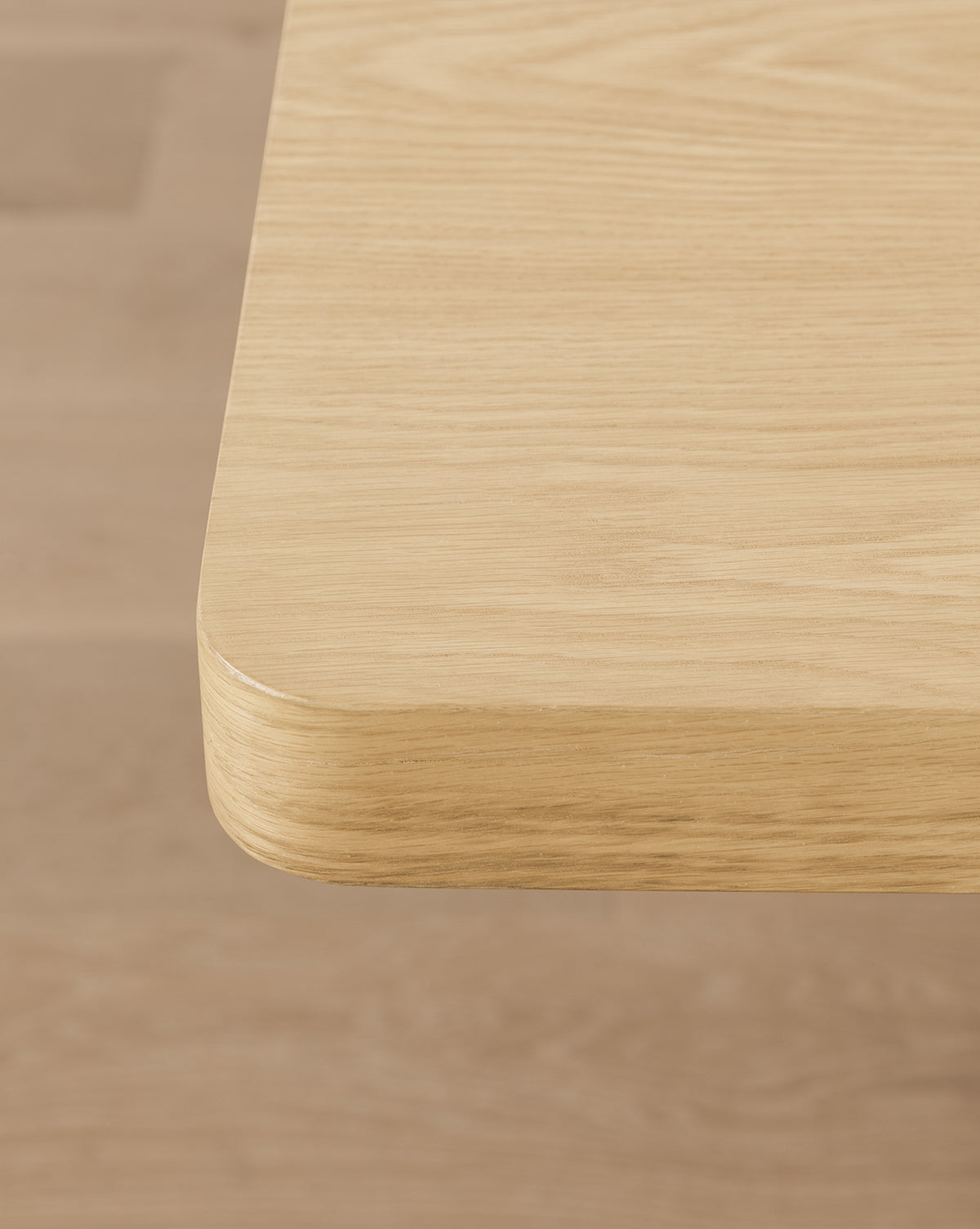 Close-up of the Wilton Dining Table’s corner, highlighting its white oak finish, rounded edges, and smooth natural grain against a matching wood floor background, by McGee & Co.