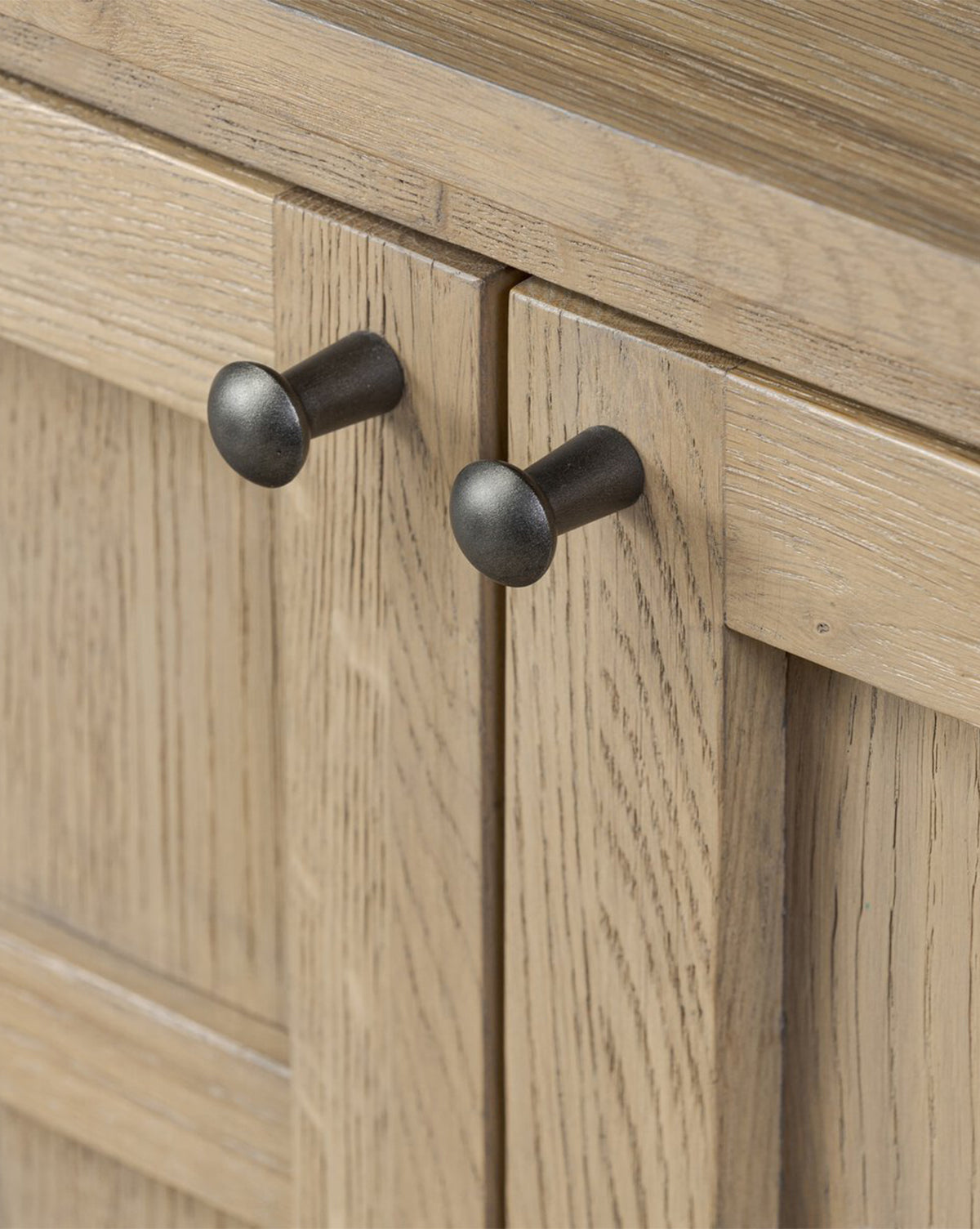 Close-up of two black round knobs on the Wynne Sideboard’s wooden cabinet doors, featuring a light natural finish and visible wood grain—a stylish accent for this solid oak sideboard, by McGee & Co.