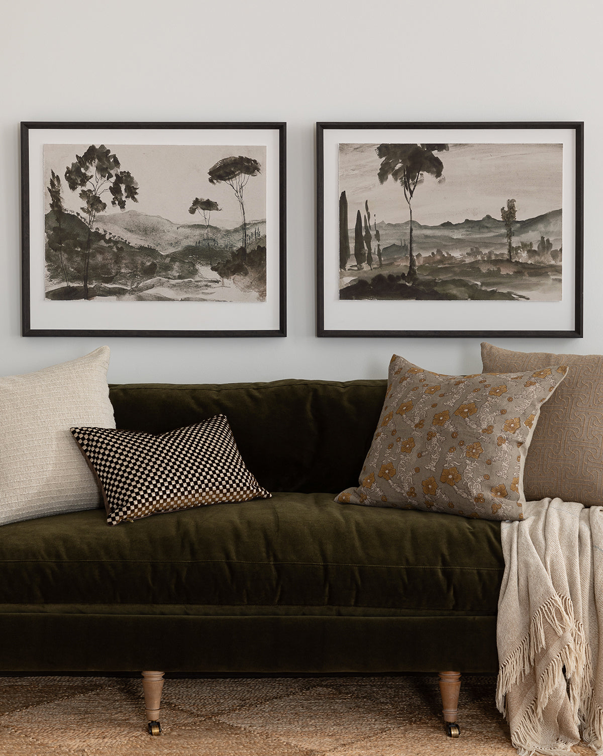 A dark green velvet sofa with patterned and neutral pillows and a light throw sits beneath the Washed Terrain II landscape watercolor art print in a black frame on a white wall.