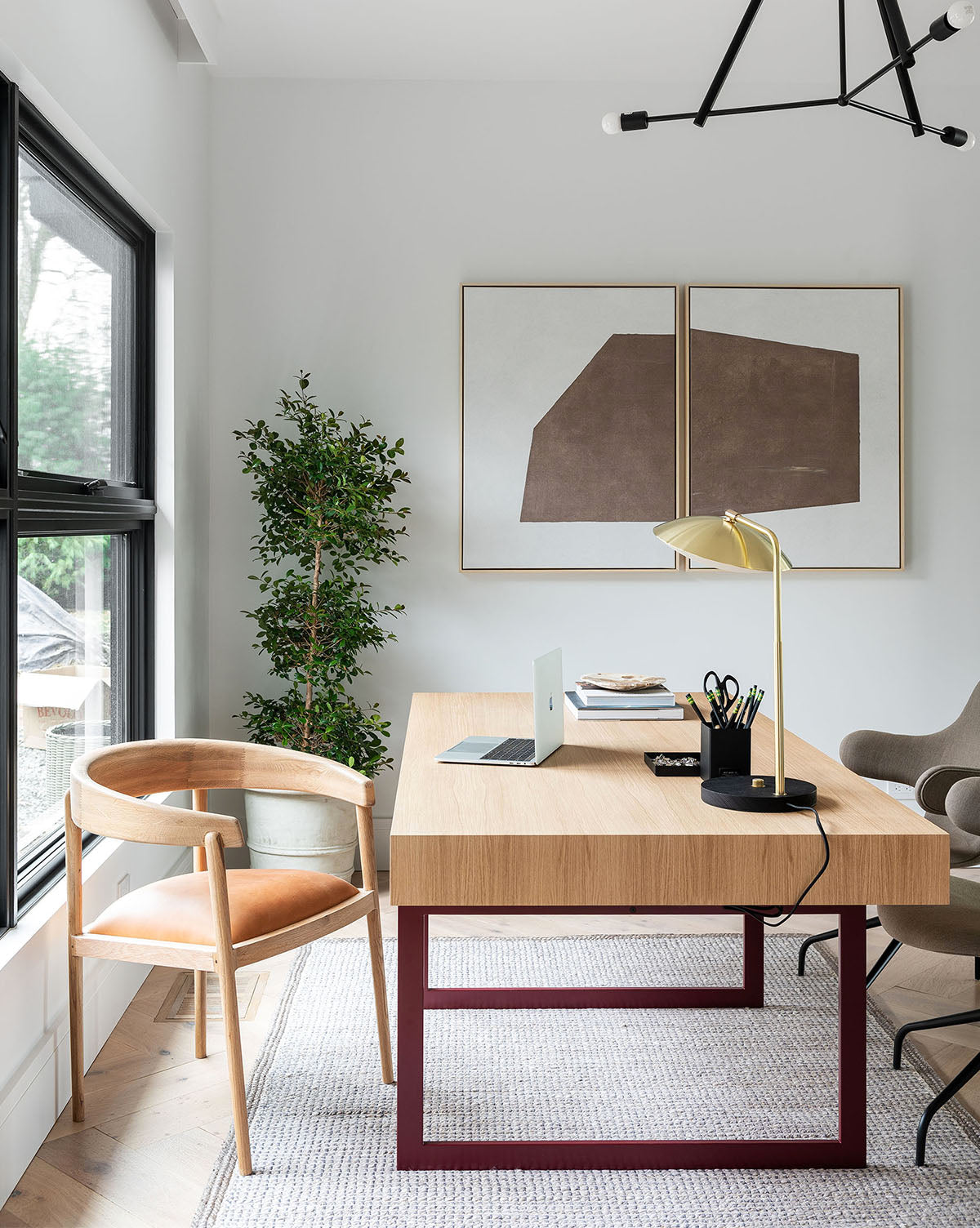 A modern home office features a light wooden desk, tan leather chair, décor, laptop, lamp, potted plant, and Entering Shape 1 taupe wall art. Large windows allow natural light to brighten the neutral-toned space.