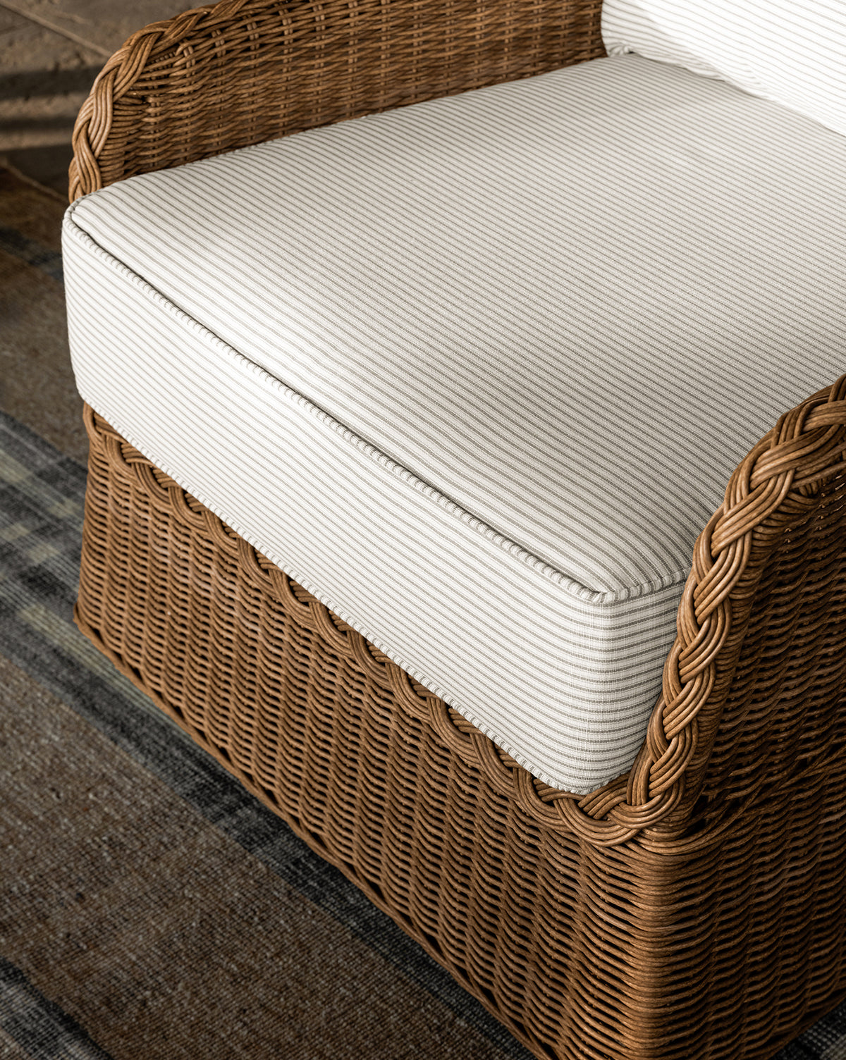 Close-up of the Haviland Outdoor Swivel Lounge Chair with a weather-resistant frame and white striped cushion, set on a dark patterned rug by McGee & Co.